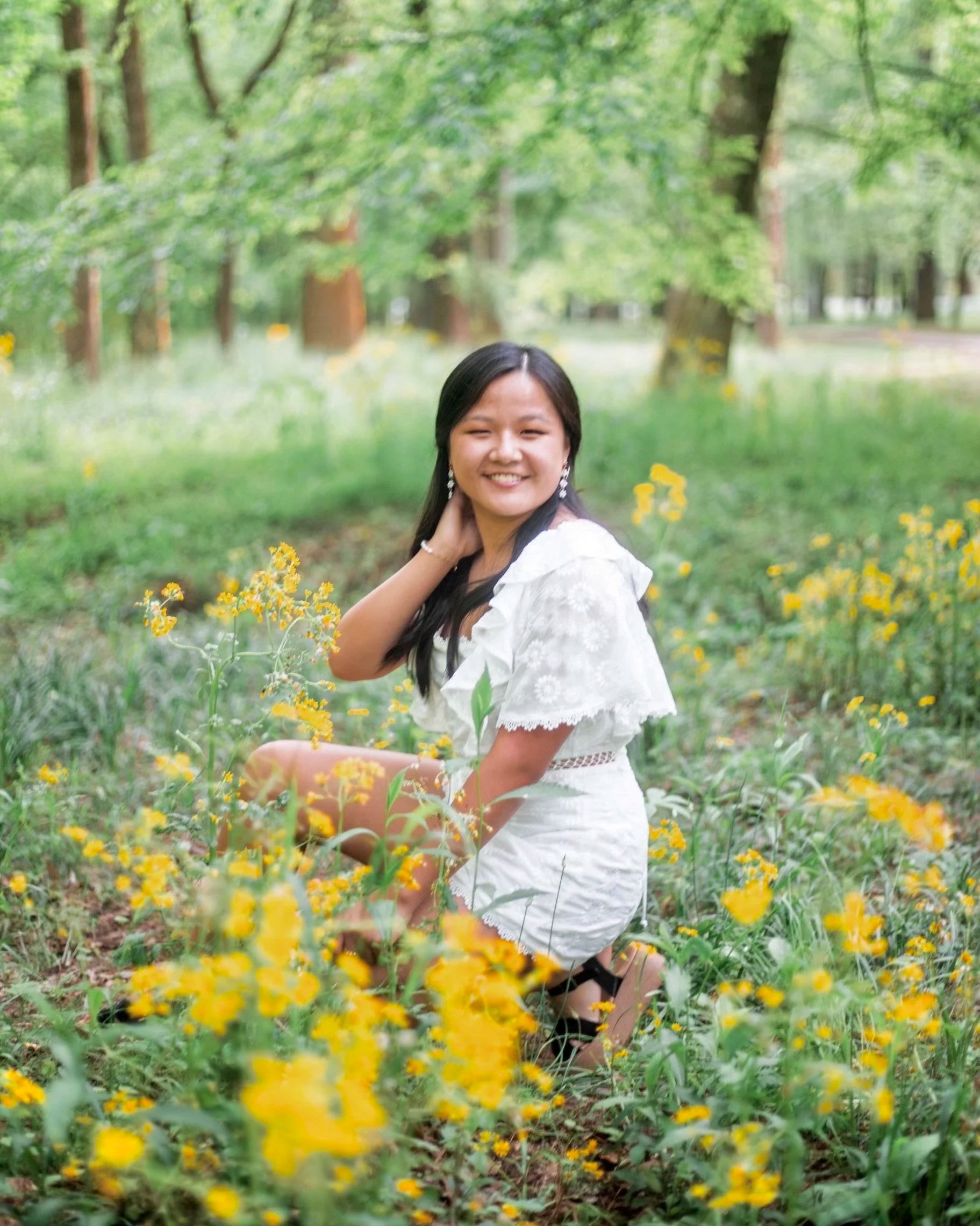 Young woman in a white dress kneeling in a field of yellow flowers in a lush green park. Lily Chambers graphic design