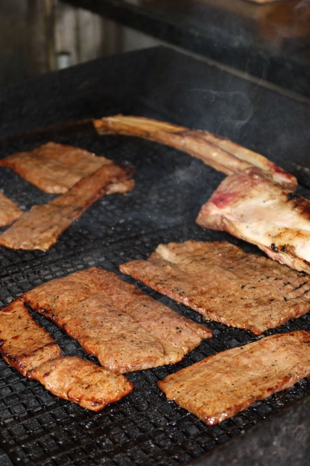 Marinated meat (short rib) with whole bone cooking on a grill with smoke coming off.