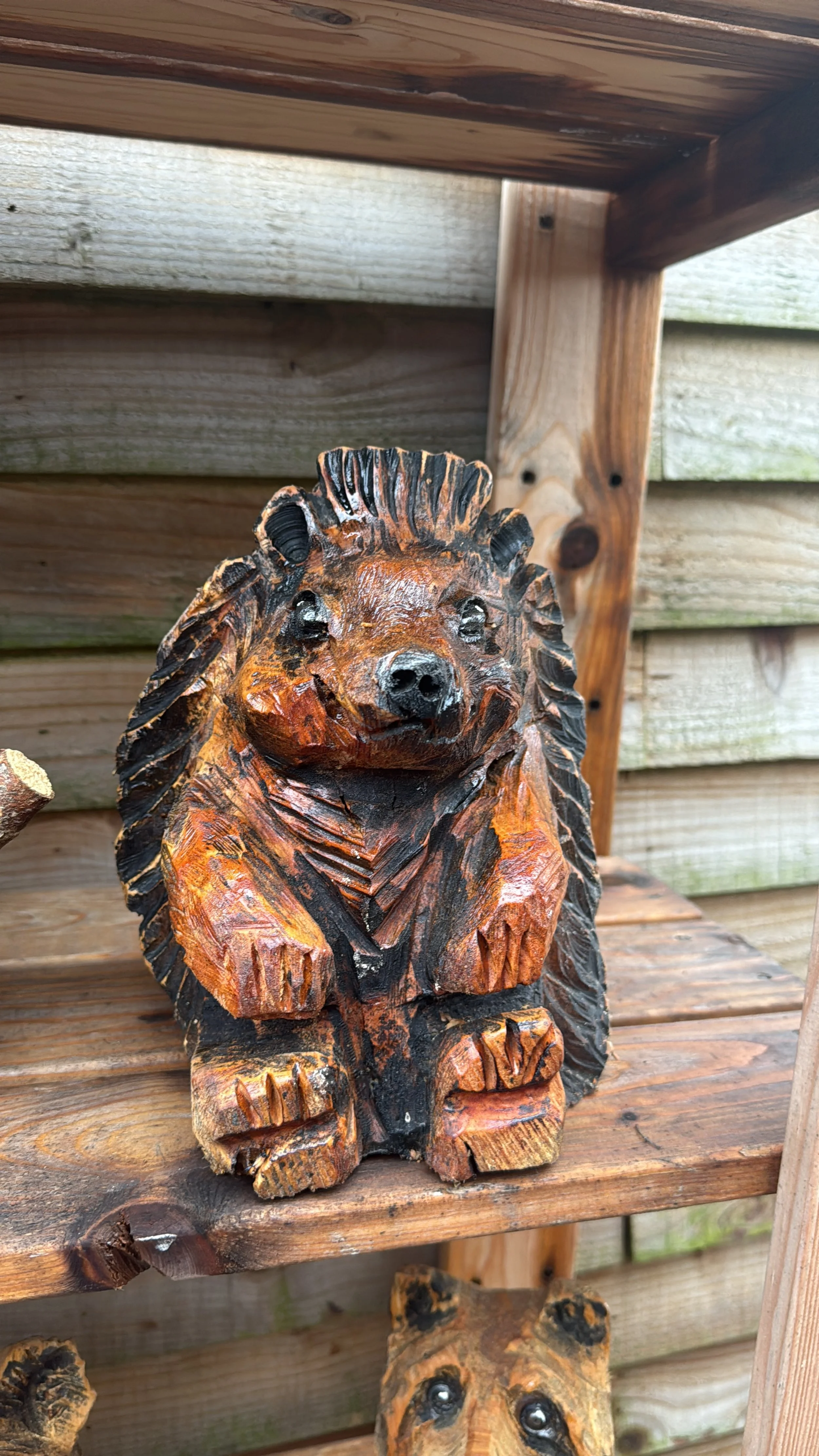 Carved wooden bear figurine sitting on a wooden shelf outdoors.
