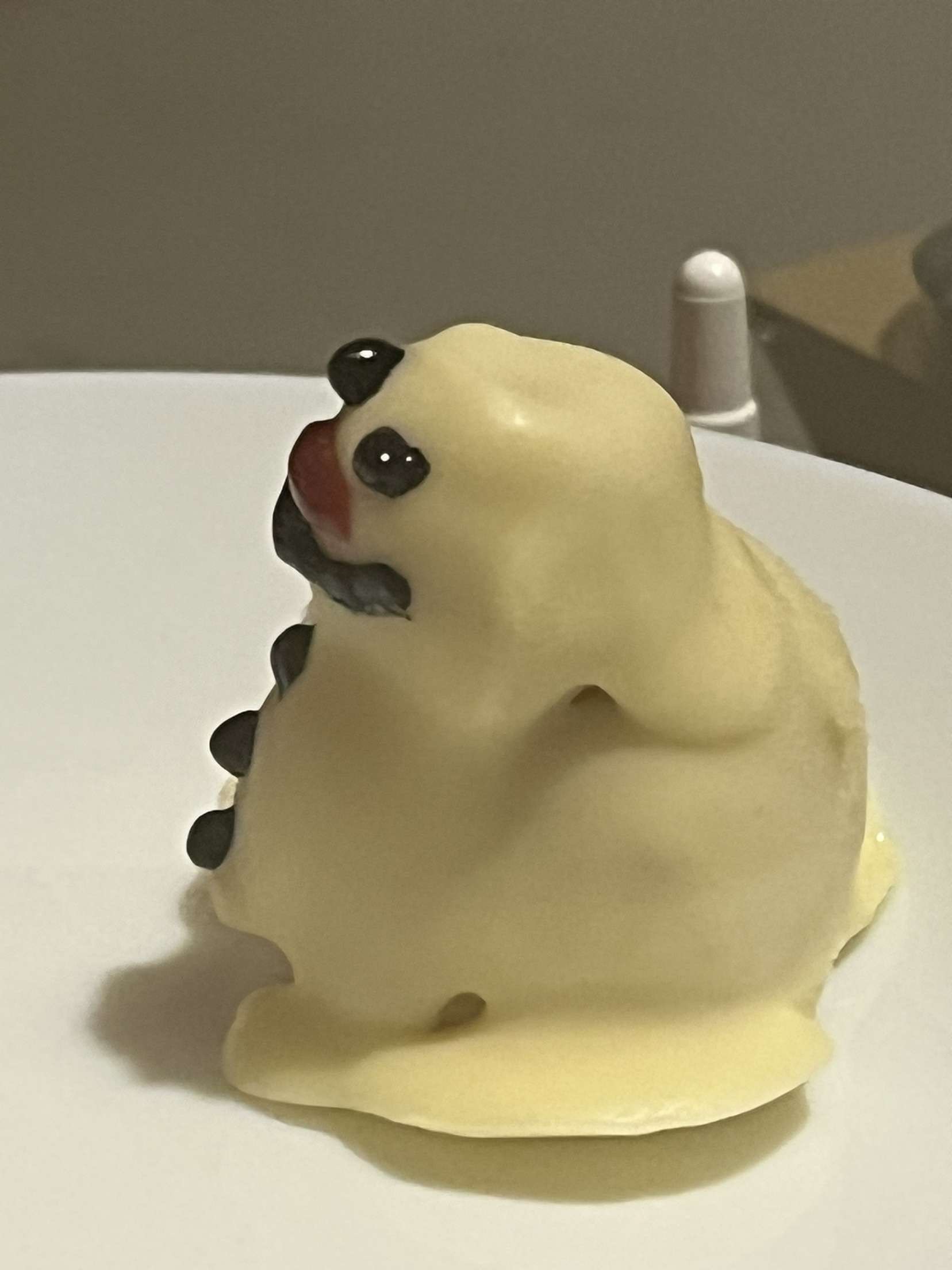 A dessert shaped like a snowman, with a white chocolate exterior, black eyes, nose, ears, and a small reddish tongue.