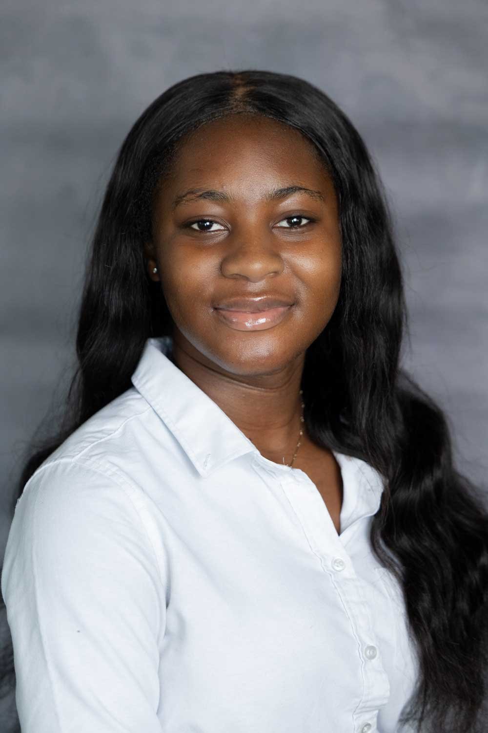A young African American woman with long black hair, wearing a white collared shirt, smiling softly against a gray background.