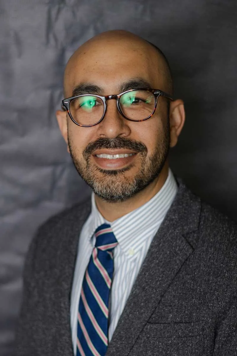 An administrator at The Cambridge School of Dallas classical Christian school grades 5-12, wearing a suit and striped tie, against a dark background.