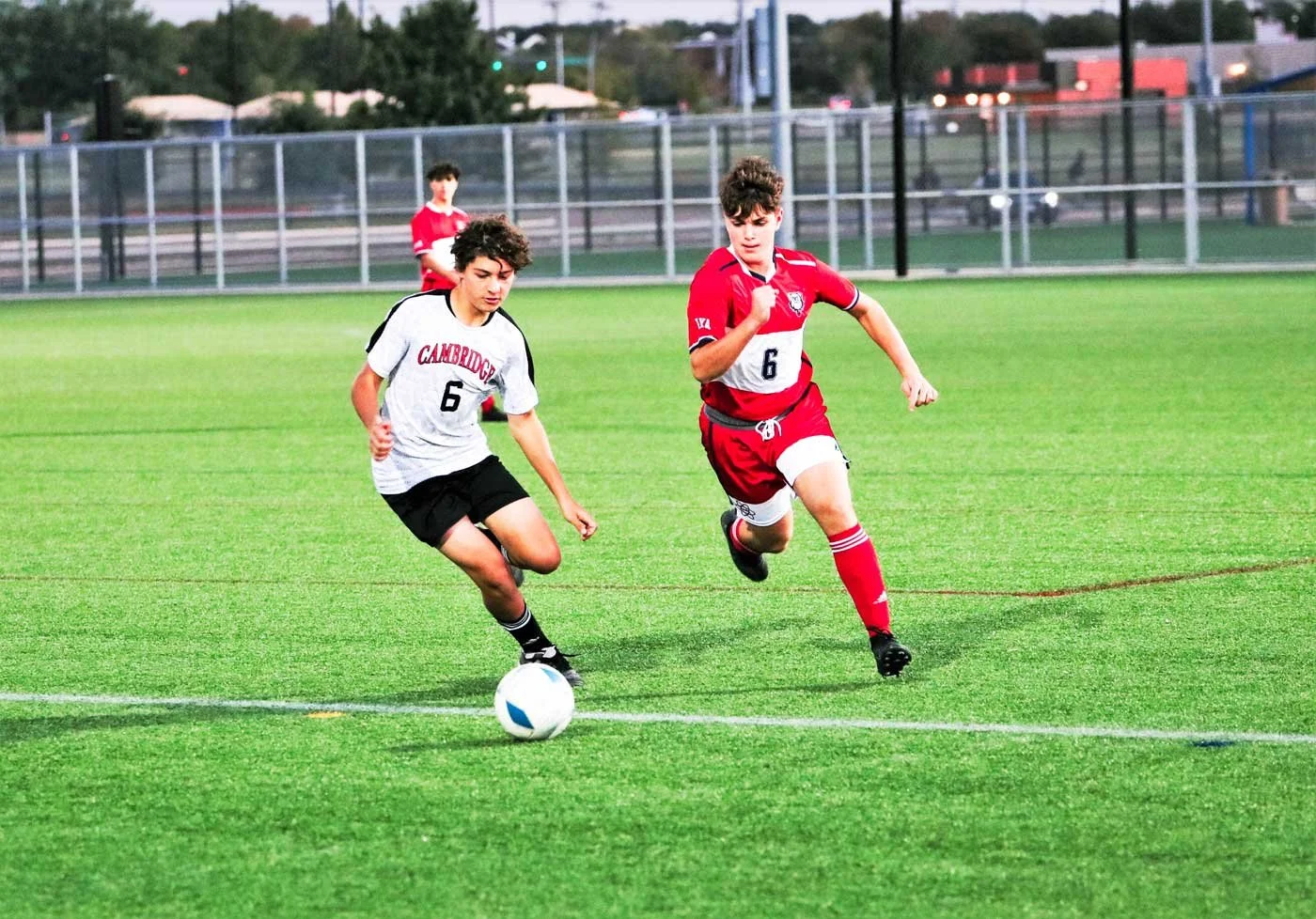 Two young male soccer players chase a ball on a green field during a game, with a teammate in the background.