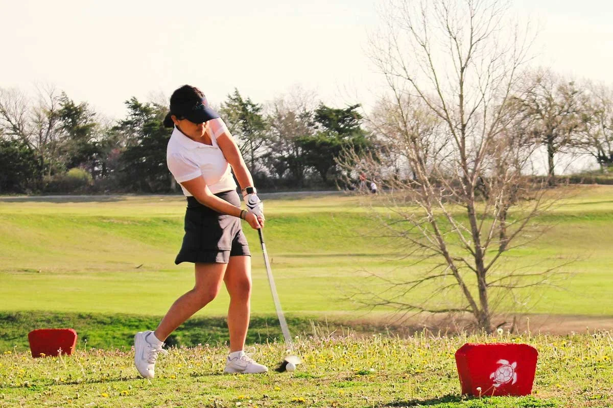 A woman playing golf on a golf course during daytime, preparing to tee off.