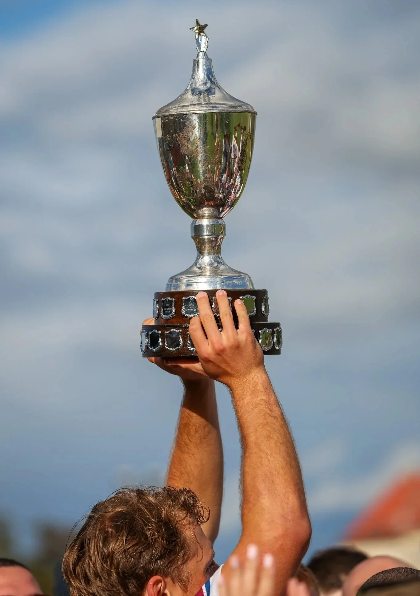 Player coach holding a trophy at an outdoor sporting event.