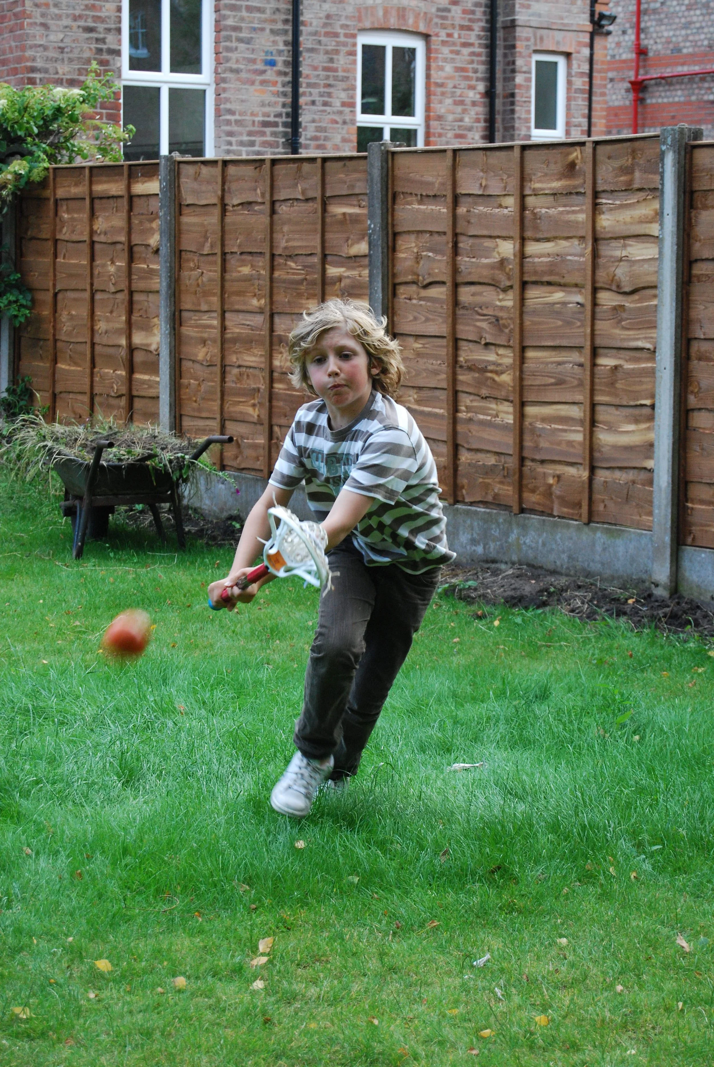 Young boy playing lacrosse in a garden.
