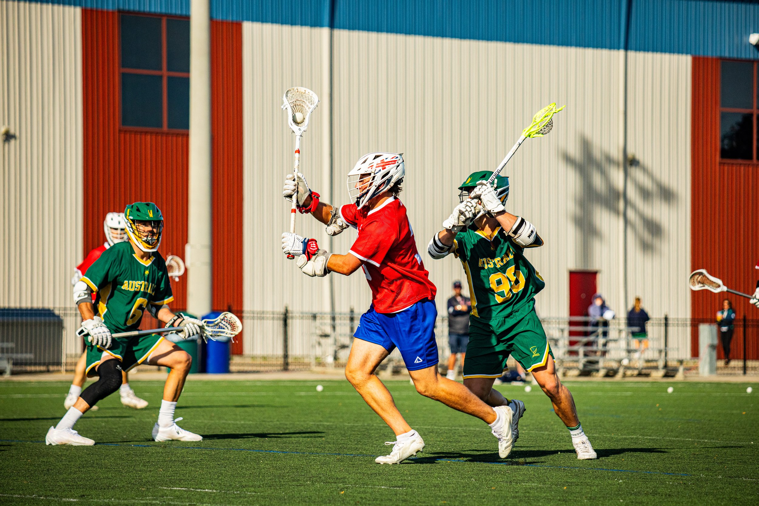 International lacrosse players competing during a match on a grass field in Canada.