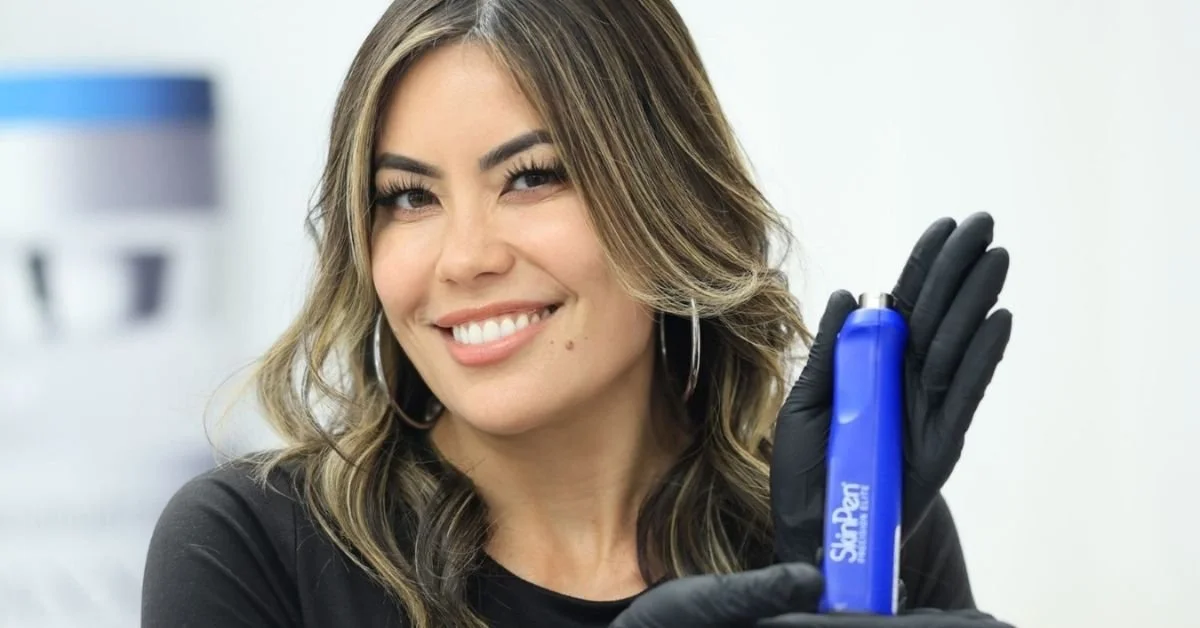 Smiling aesthetician holding SkinPen device used in microneedling skin treatment.