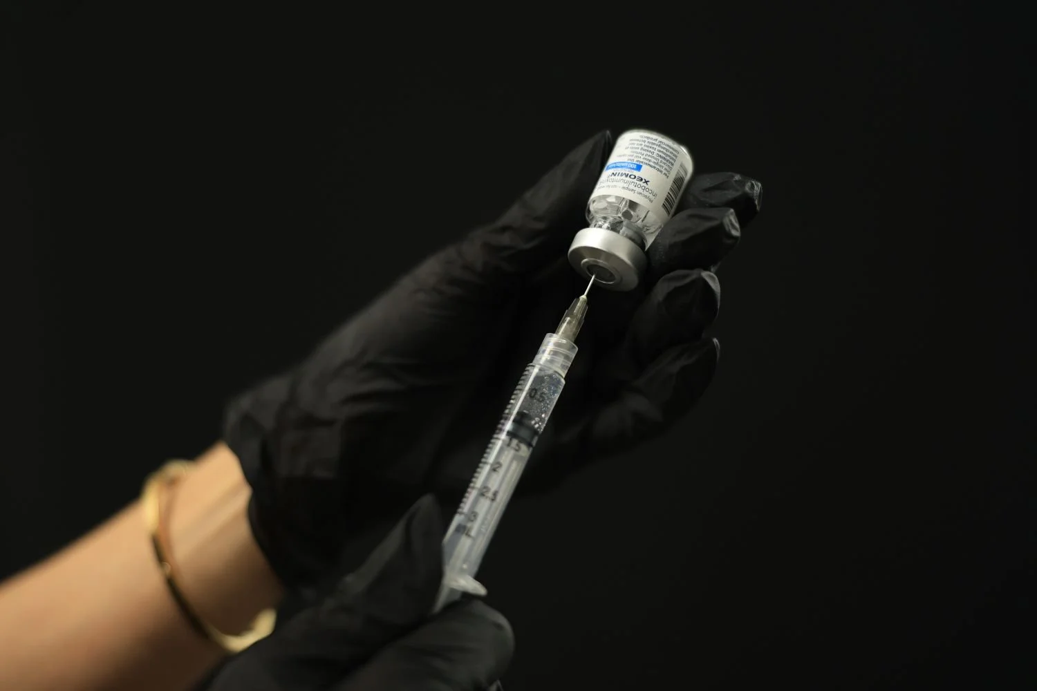 A pair of gloved hands holding injection needle while drawing up a vial of Xeomin.
