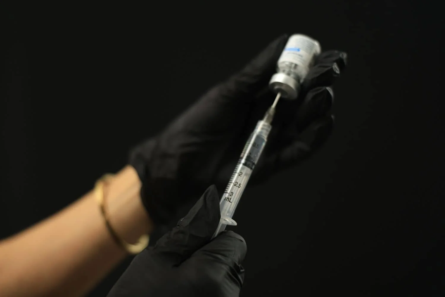 Gloved hands drawing hyaluronidase from a vial into a syringe for dissolving filler.