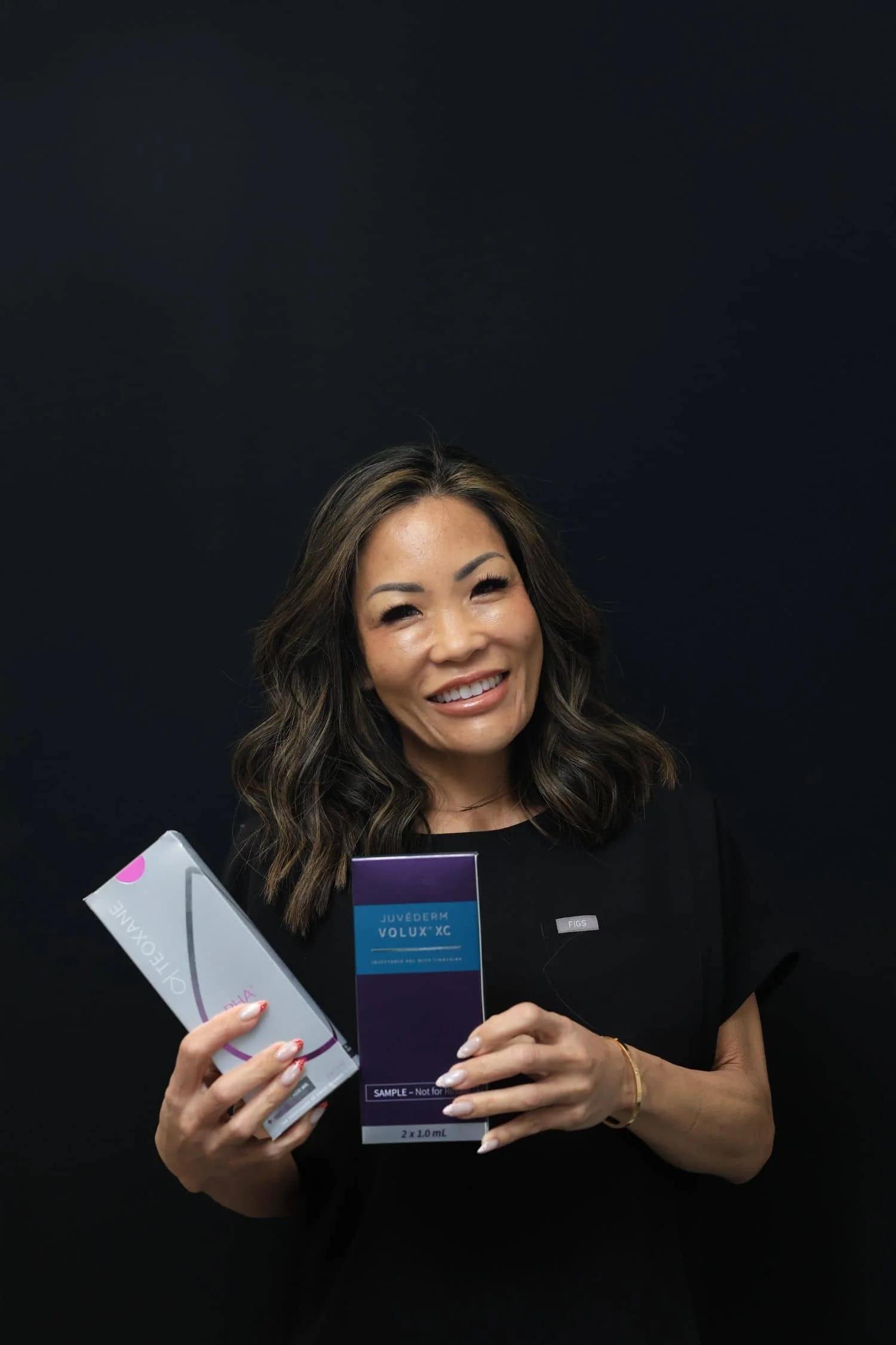 Aesthetic injector smiling while holding filler products as part of a personalized filler correction treatment plan.