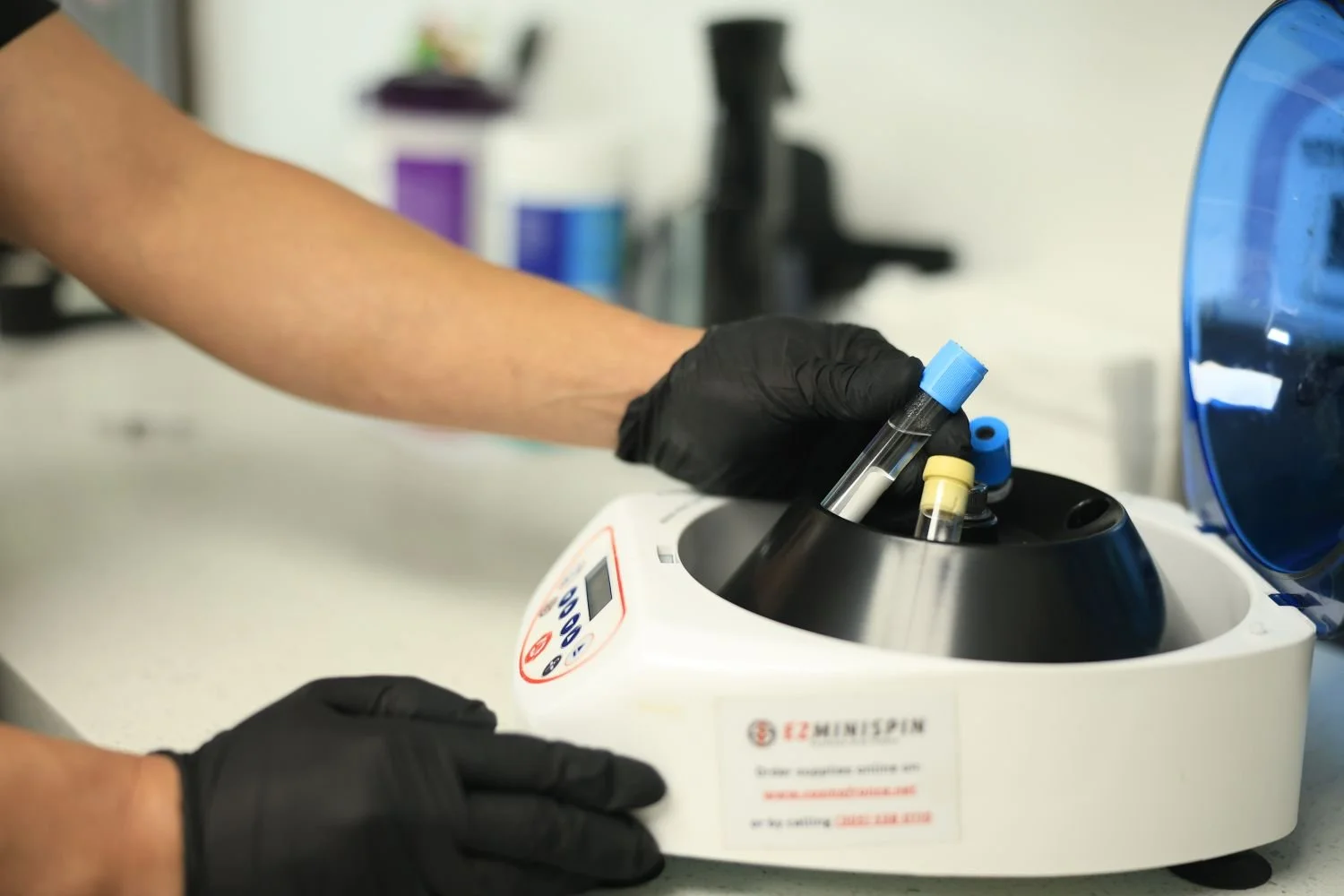 A man wearing gloves while taking out vials out of a blood spinning machine for medical aesthetic use.