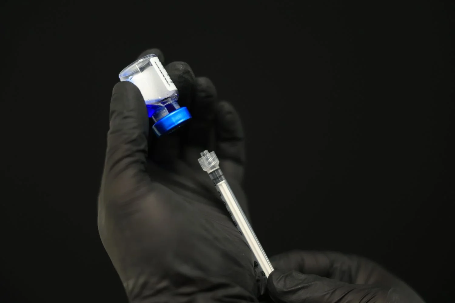 Gloved hands filling an injection needle with dermal filler.