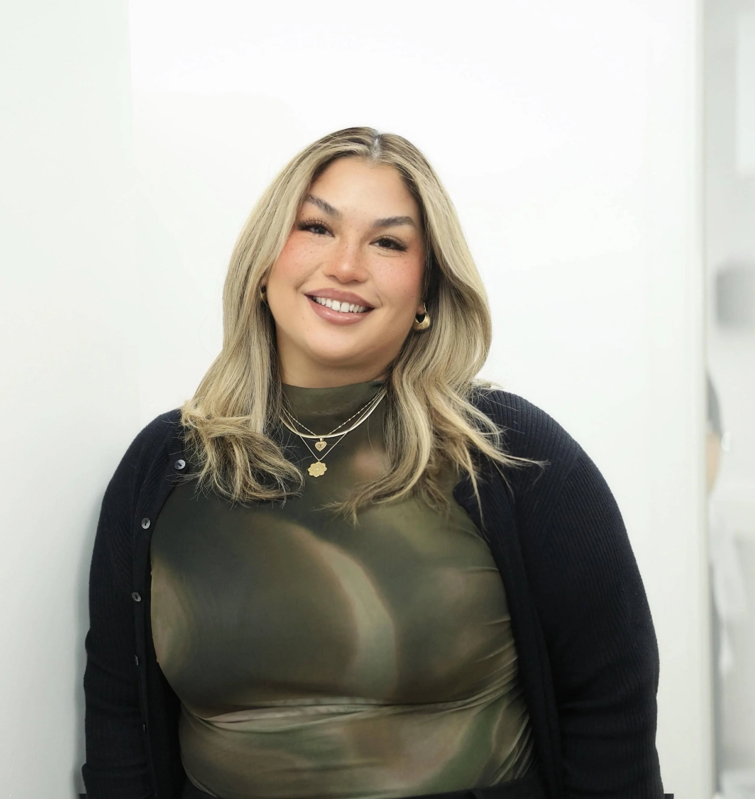 A woman with blonde hair wearing a green top and black cardigan smiling at the camera.