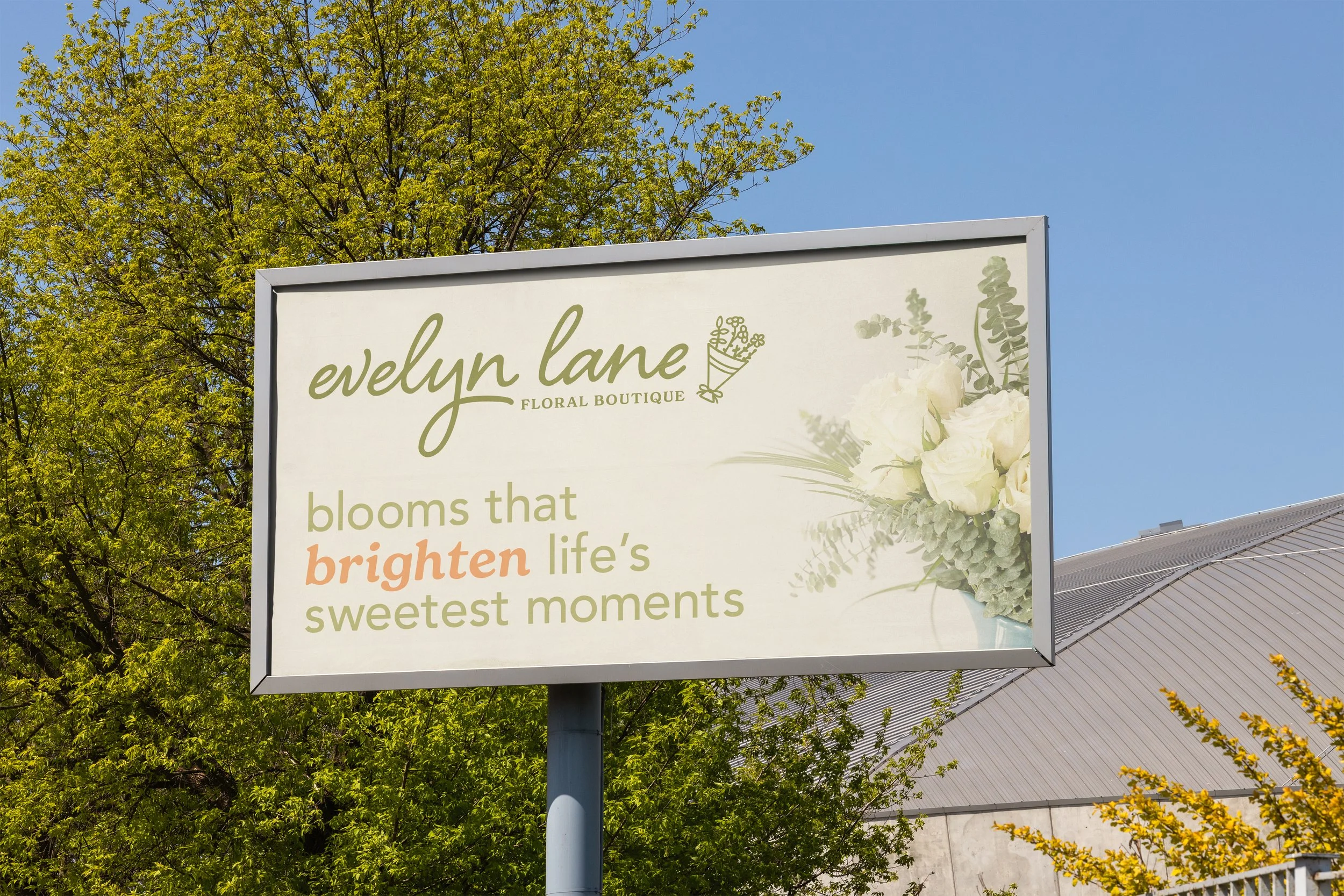 Billboard for Evelyn Lane Floral Boutique with white roses and greenery, against a blue sky and green trees.