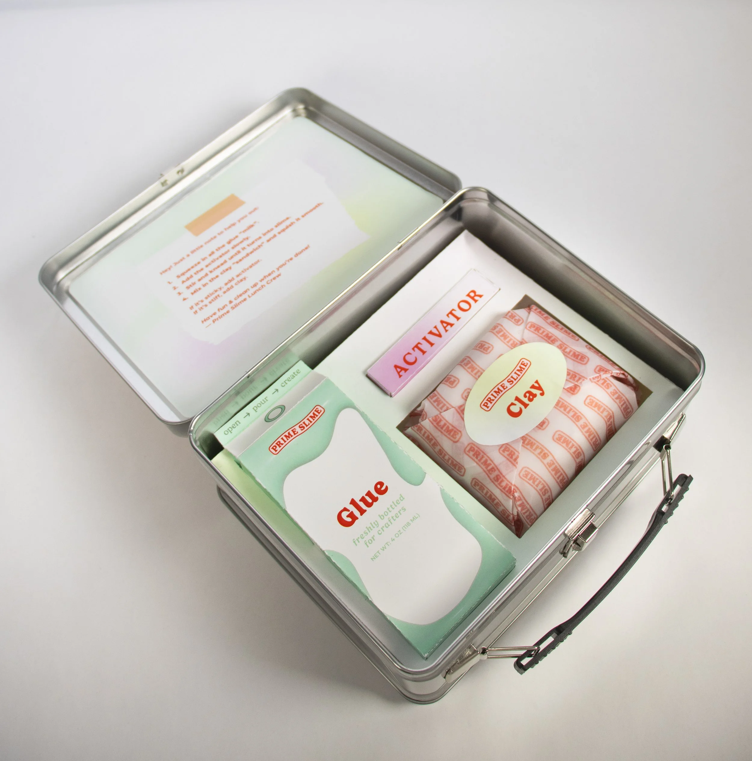 A metal box containing slime-making supplies, including a package of clay, a bottle of glue, and a stick labeled 'Activator.'