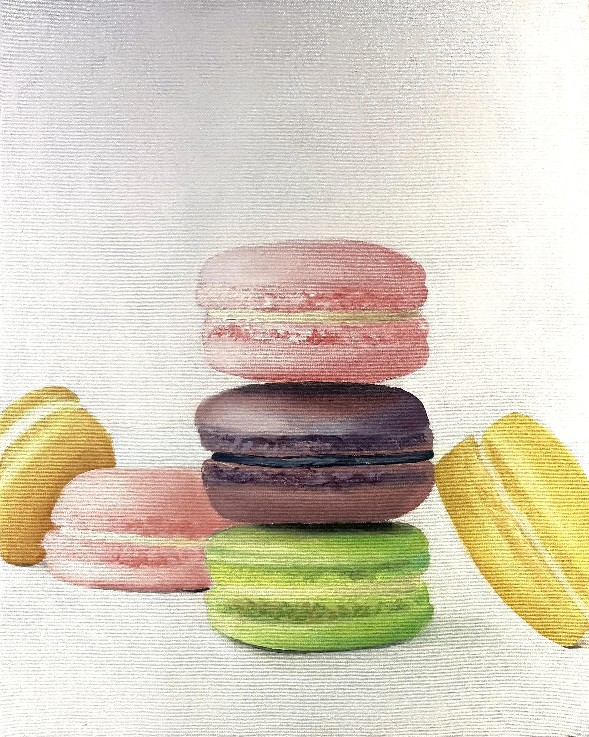 Four colorful macarons stacked vertically, with two yellow macarons on either side and a pink macaron at the bottom.