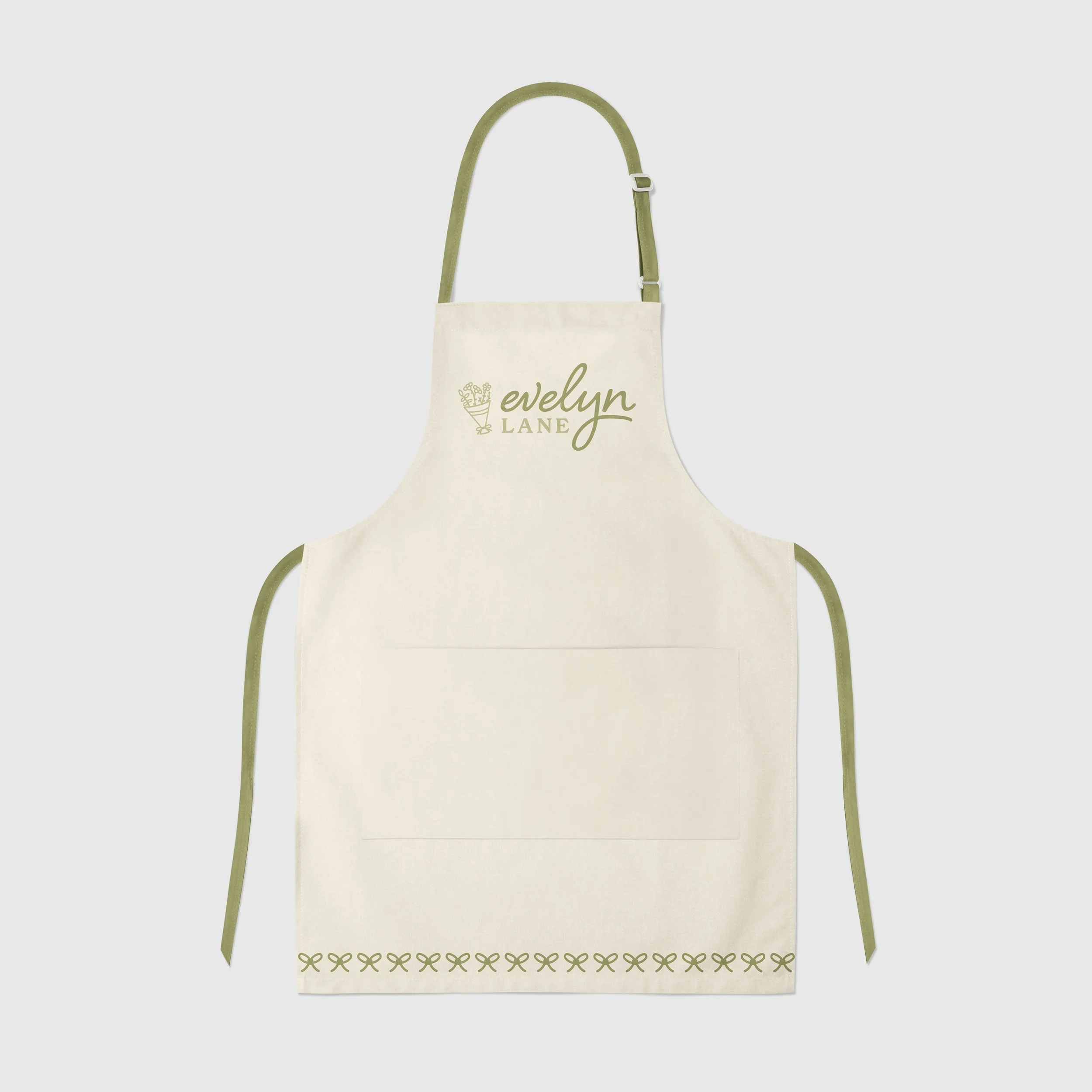 Cream-colored apron with green straps, embroidered with the words 'Evelyn Lane' and a small flower arrangement logo on the chest, and a decorative border at the bottom.