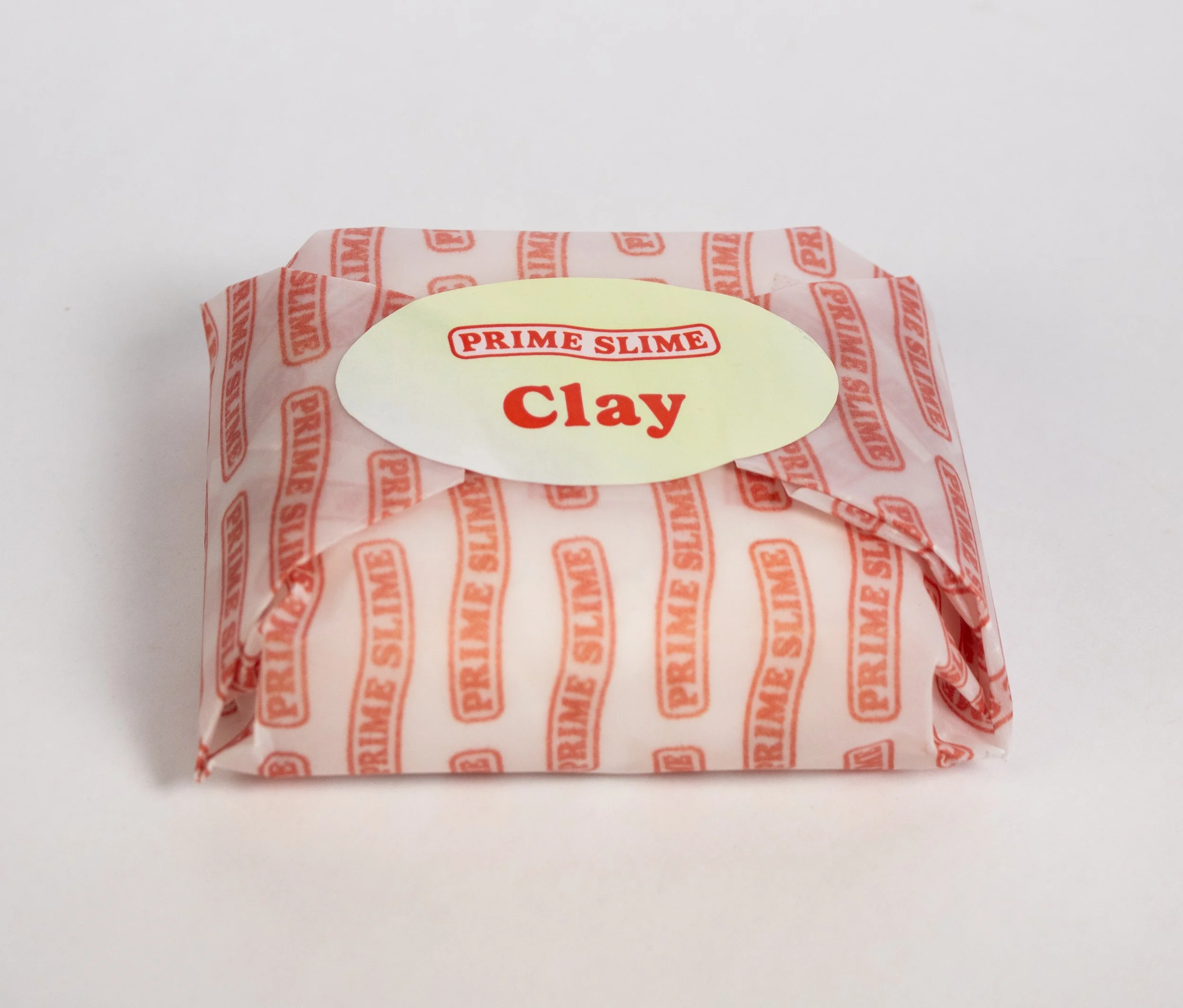 A small package of Prime Slime clay wrapped in white and red branded paper with an oval label on top reading 'Prime Slime Clay'.