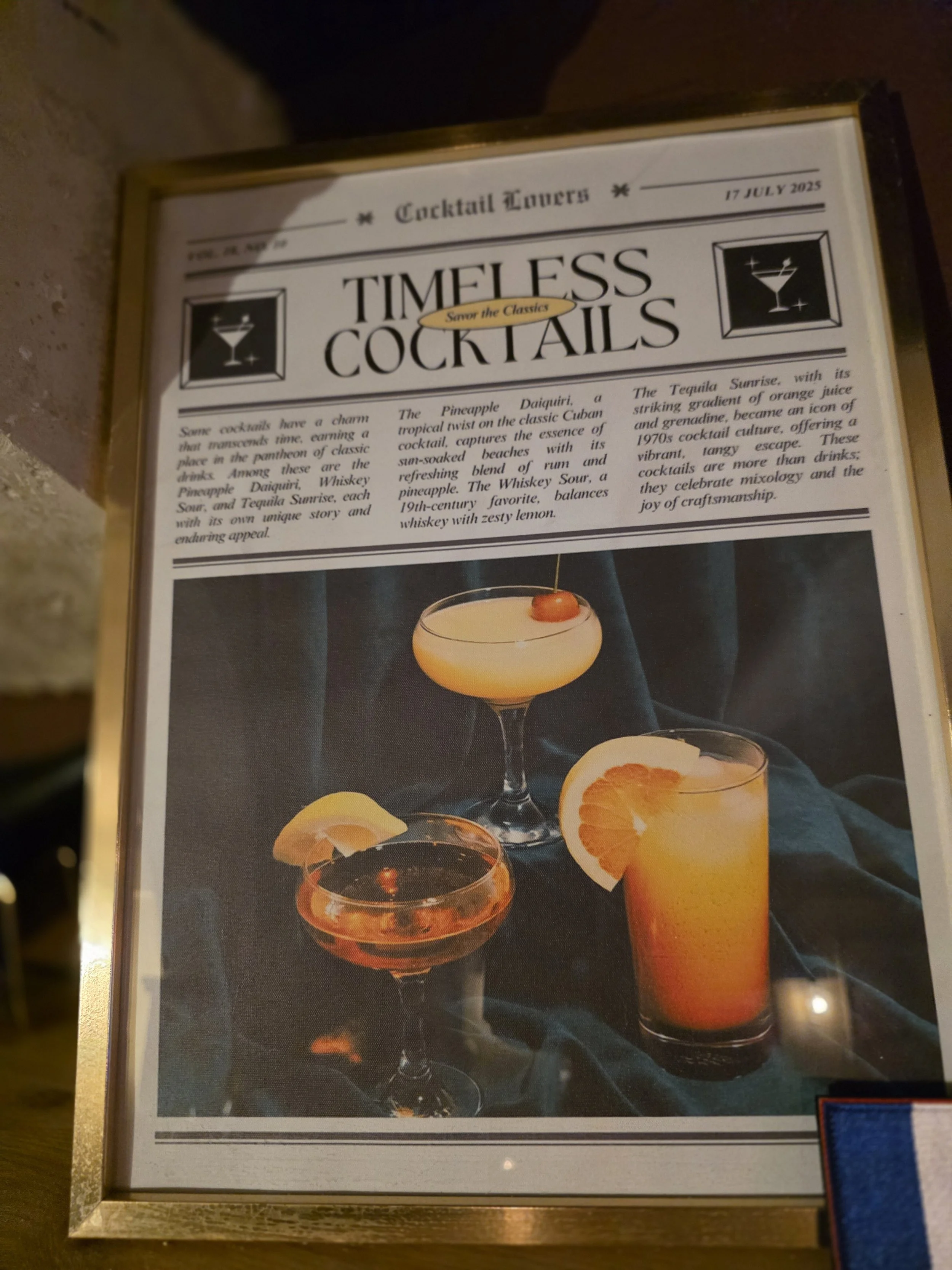 Menu sign titled "Timeless Cocktails" with text description and images of three different colorful cocktails with fruit garnishes.
