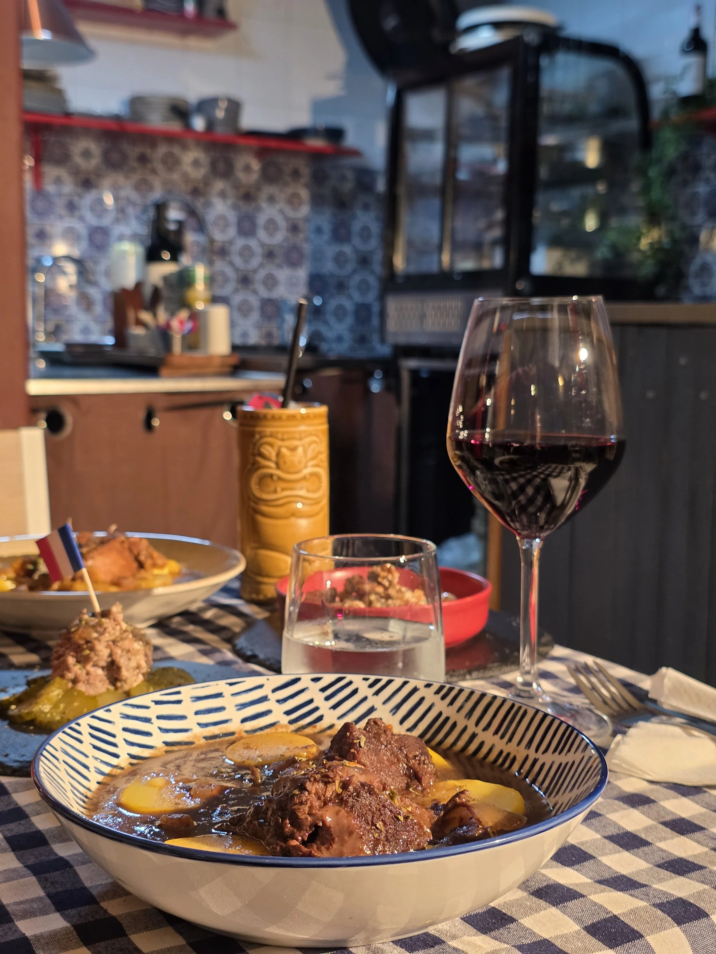 Table set with savory dishes, including beef stew with potatoes, a glass of red wine, and a glass of water, in a cozy kitchen or dining area.