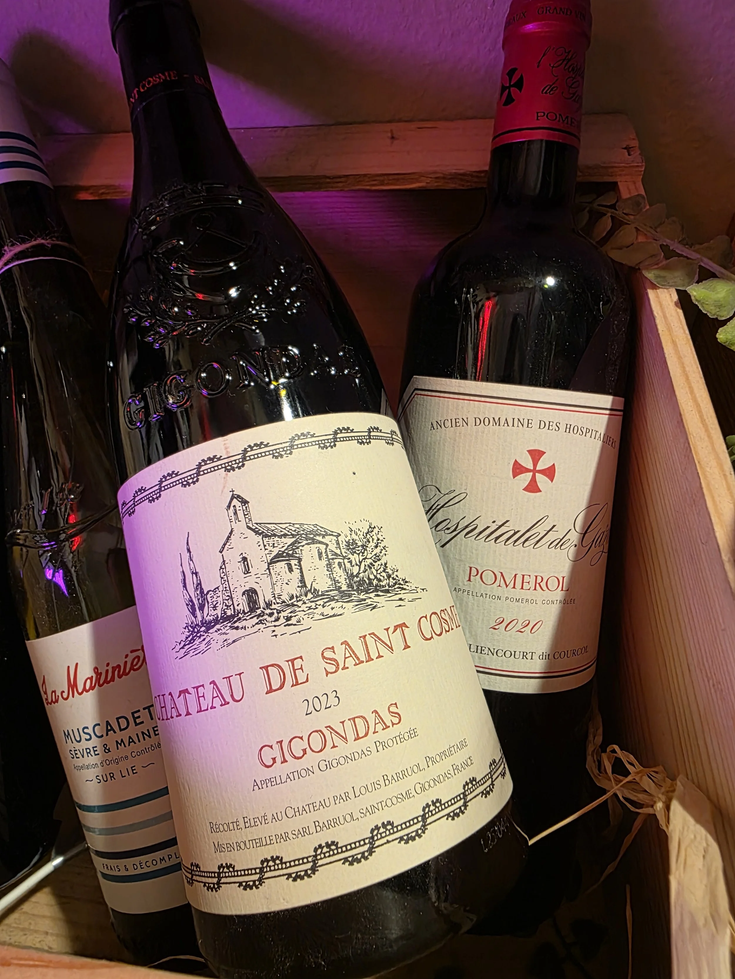 Three bottles of French wine in a wooden crate, with the focus on the middle bottle labeled 'Chateau de Saint Cosme Gigondas 2023'.