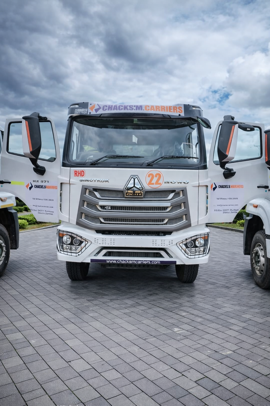 Front view of a white heavy-duty truck with open driver and passenger doors, displaying a grille with the DMC logo, chrome accents, and various stickers including the number 22, company name, and website.
