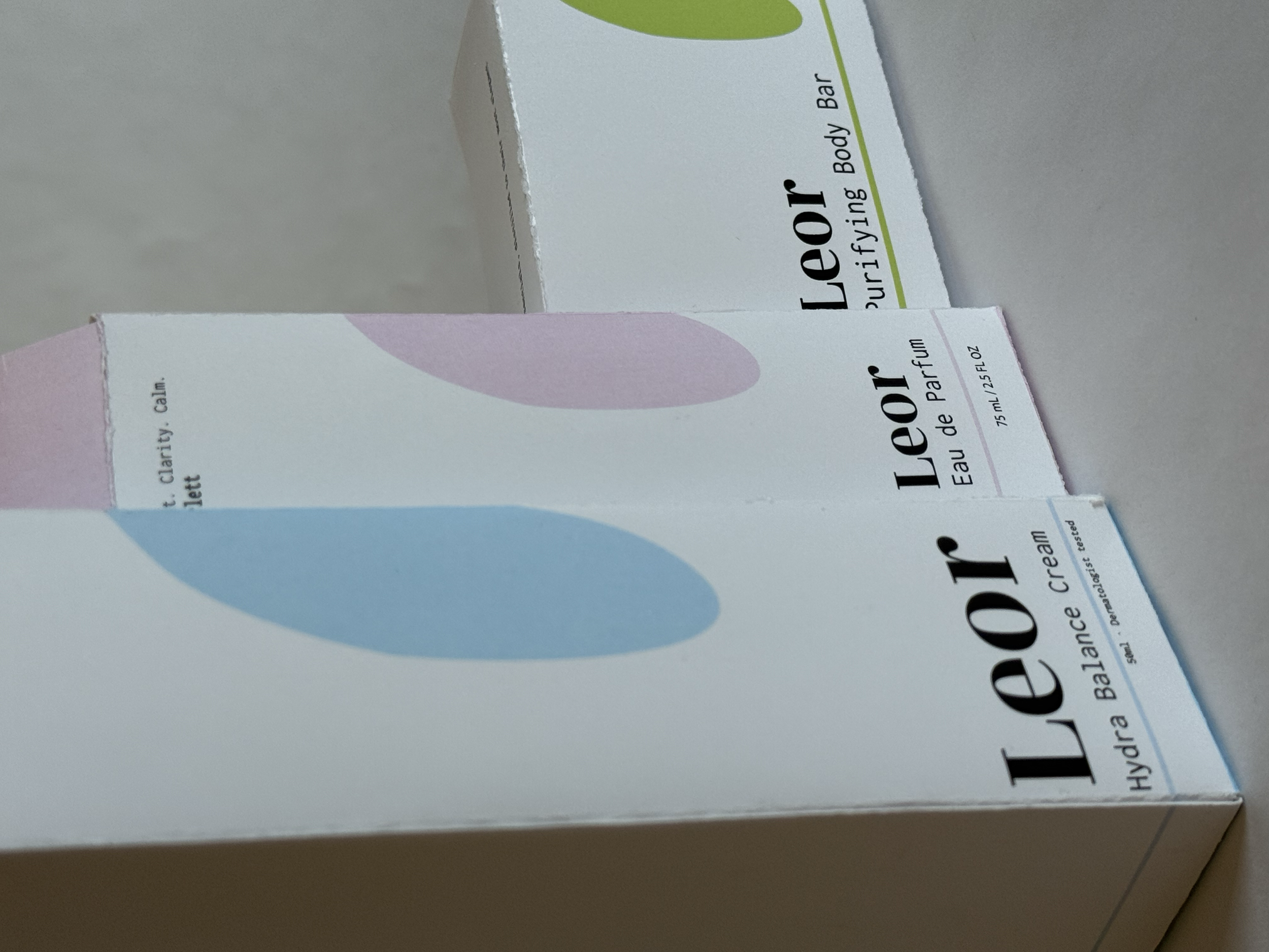 Two boxes of Leoil Hydra Balance Cream and Leoil Hydra Balance Perfume on a light gray surface. The boxes have pastel-colored abstract shapes and product information printed on them.