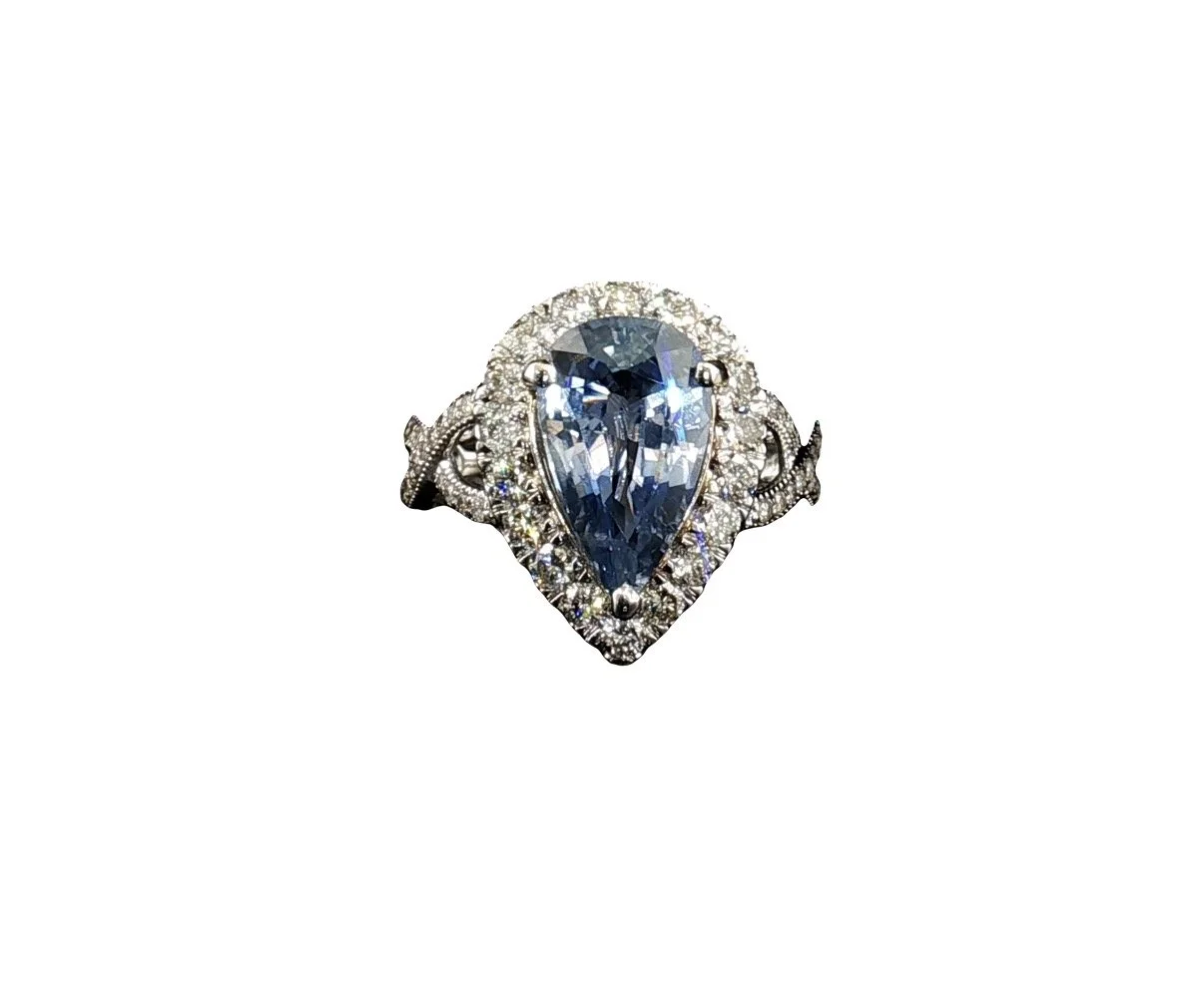 A silver ring with a teardrop-shaped blue gemstone surrounded by small diamonds.