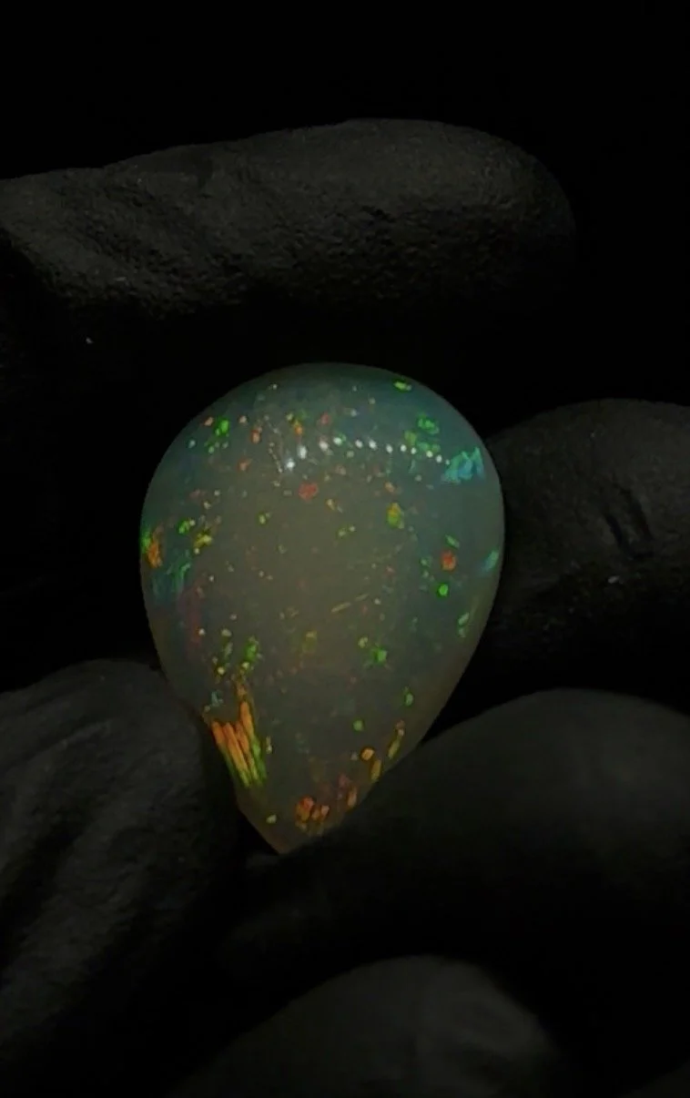 A close-up of an opal gemstone reflecting rainbow-like colors, resting on dark rocks.
