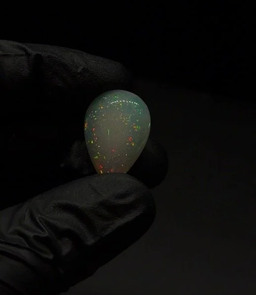 A hand wearing a black glove holding a polished opal gemstone against a black background.