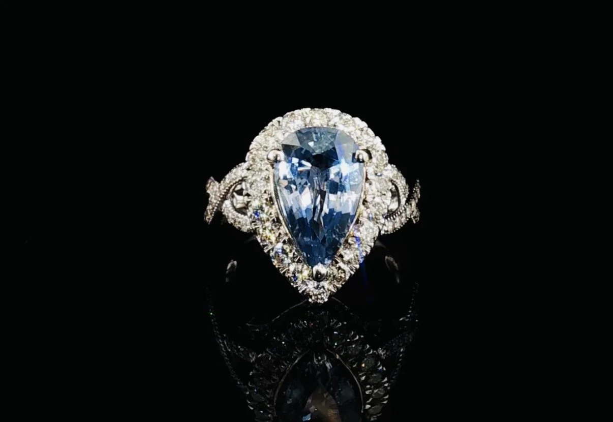 Elegant ring with a large pear-shaped blue gemstone surrounded by smaller white diamonds on a black reflective surface.