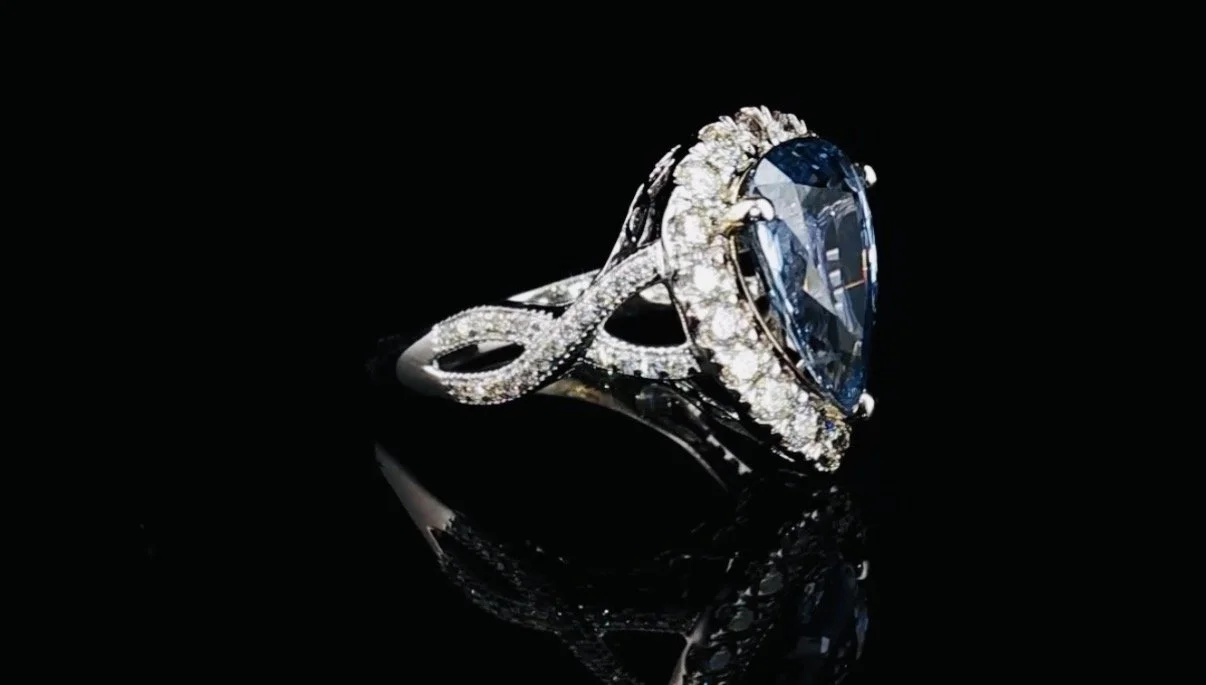 A silver ring with a large blue gemstone and small diamonds on a black reflective surface.