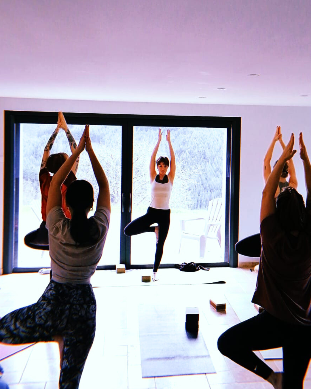 Groupe de personnes pratiquant le yoga dans une pièce lumineuse, avec vue sur un paysage enneigé à travers une grande fenêtre