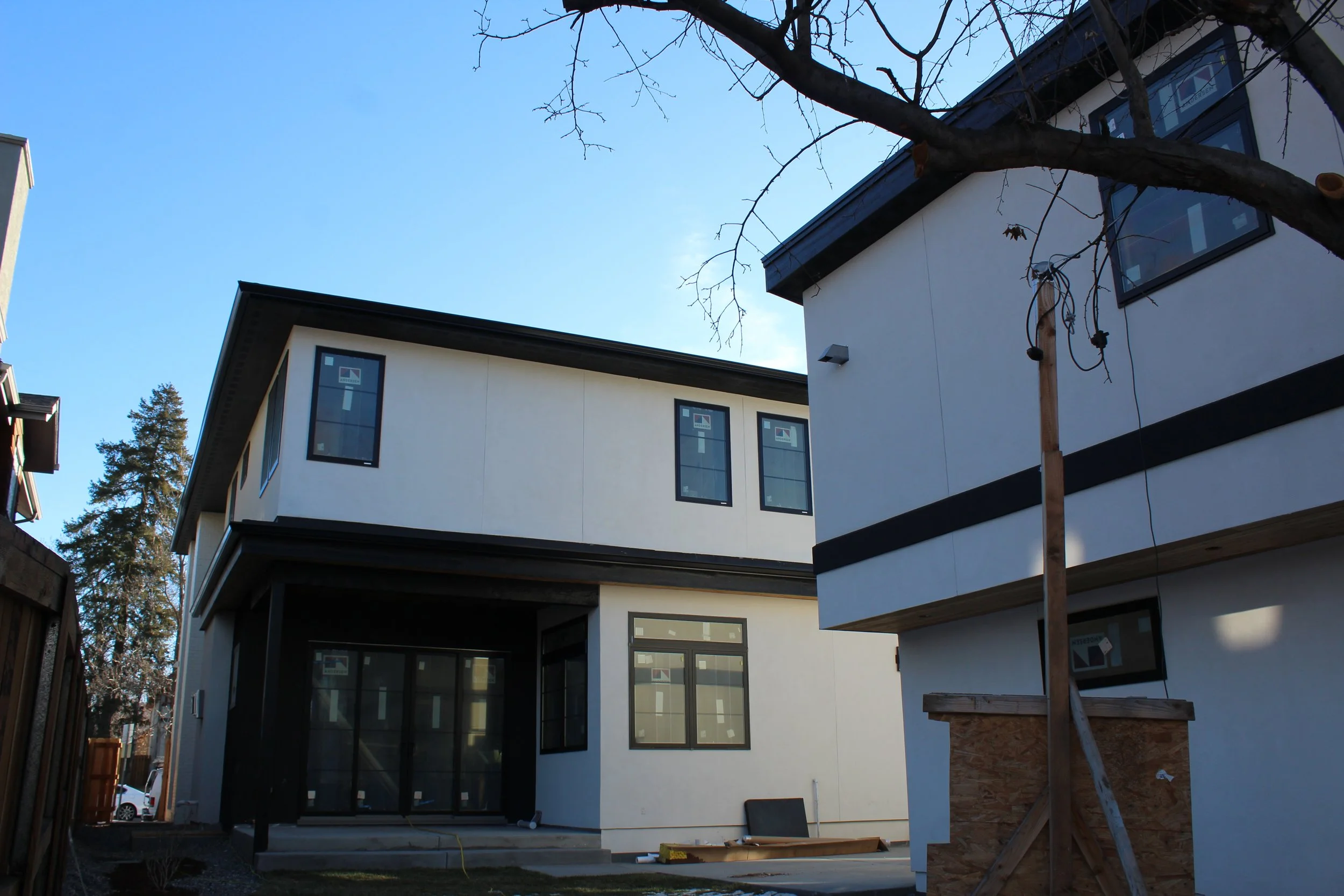 Newly constructed white two-story house with black trim, large windows, and a small front yard. Building materials are visible, and a wooden support beam is in mid-assembly in the foreground. A professional and super detailed work with premium materi