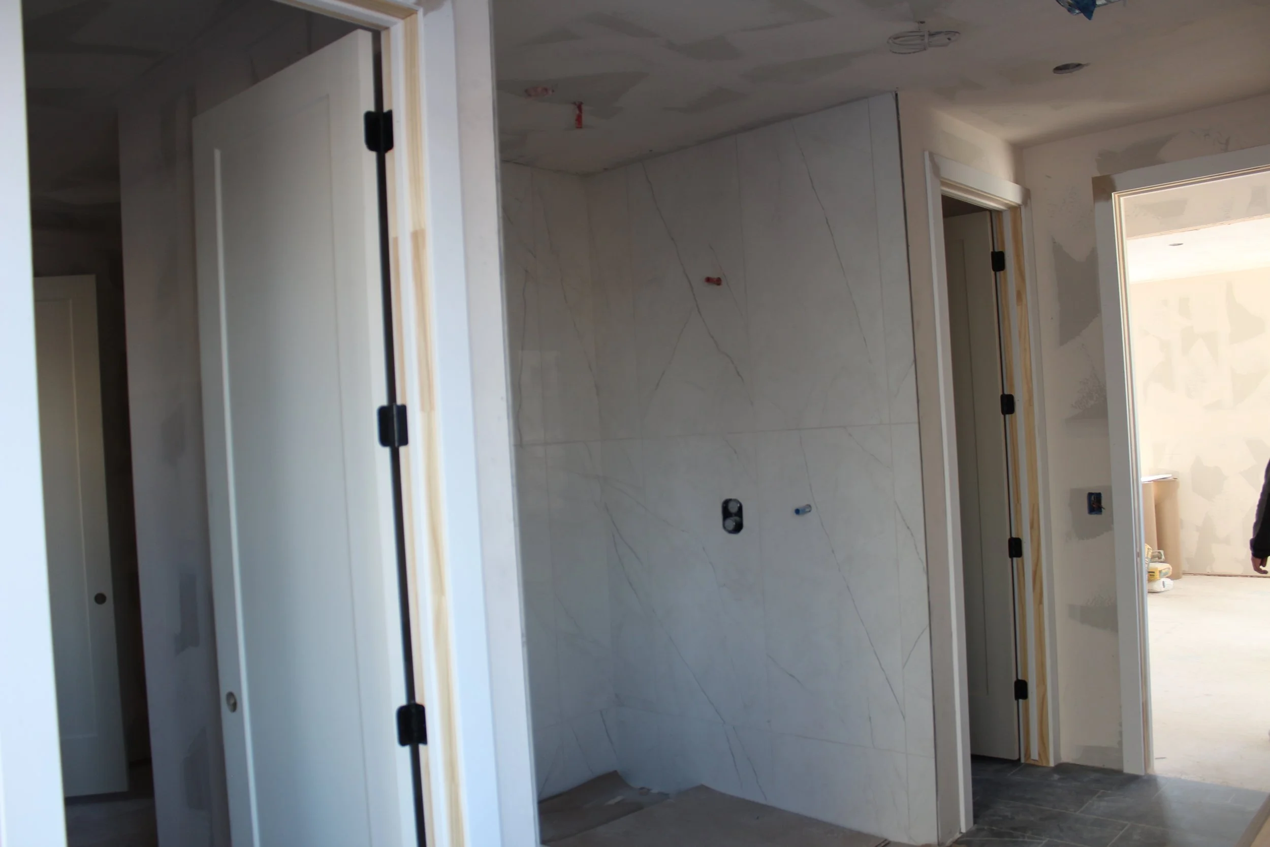 Interior of a building under construction with partially finished walls, an open doorway, and construction materials visible in the background.