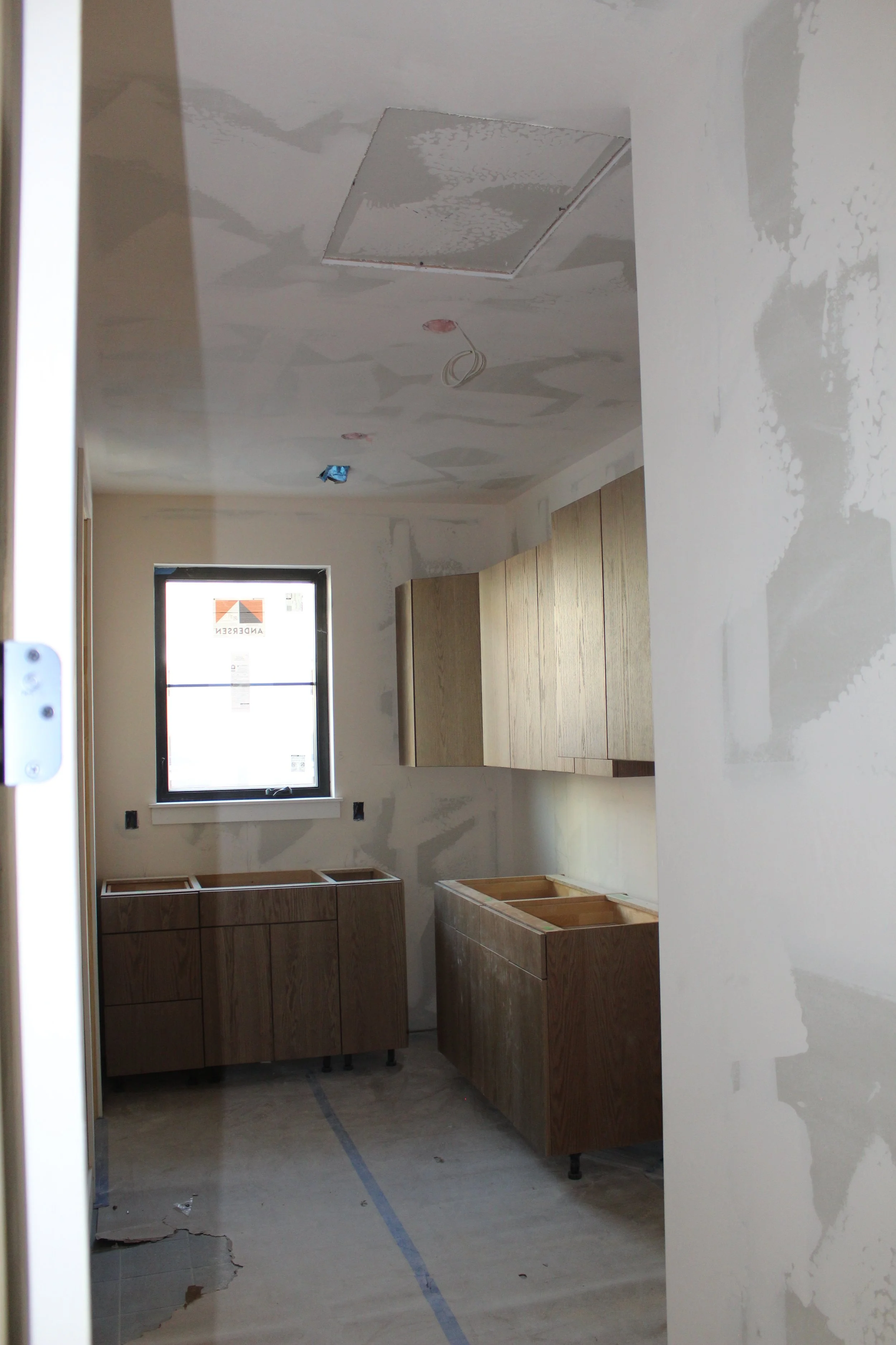 Kitchen under construction with unfinished cabinets, a window, and drywall with patching.