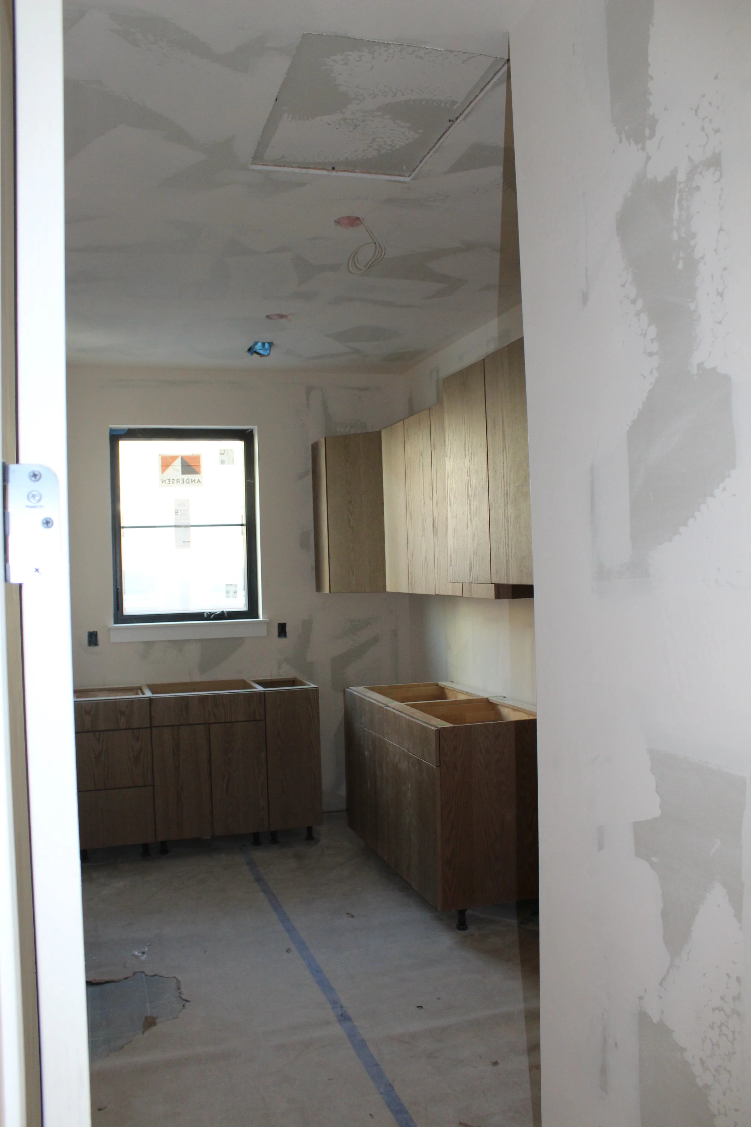 Kitchen under construction with unfinished wooden cabinets and a window, drywall with patches, and electrical wiring visible.