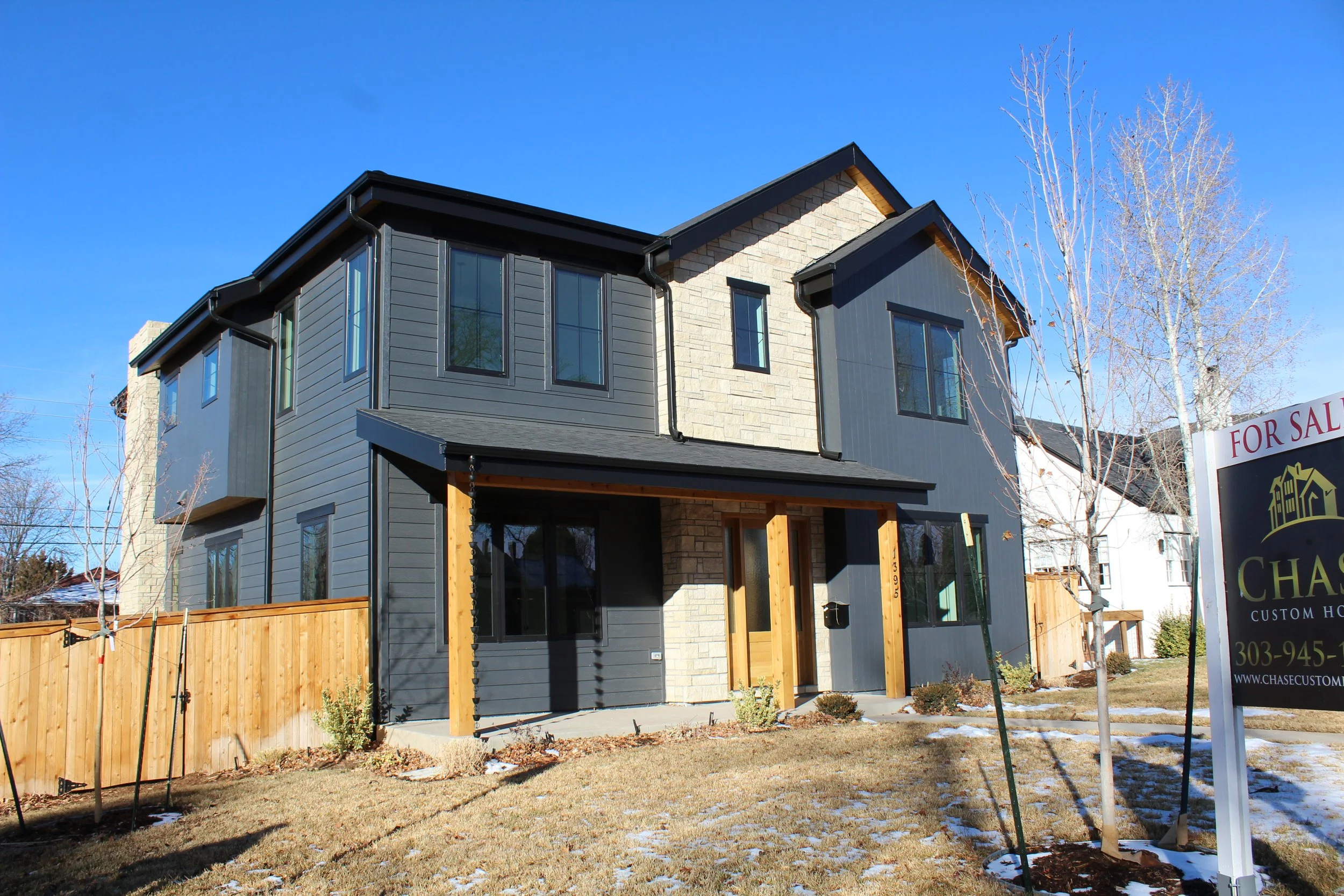 New two-story house with dark gray and light gray exterior siding, stone accents near the entrance, black framed windows, wooden front porch, and a sign indicating it is for sale A professional and super detailed work with premium materials. This is 