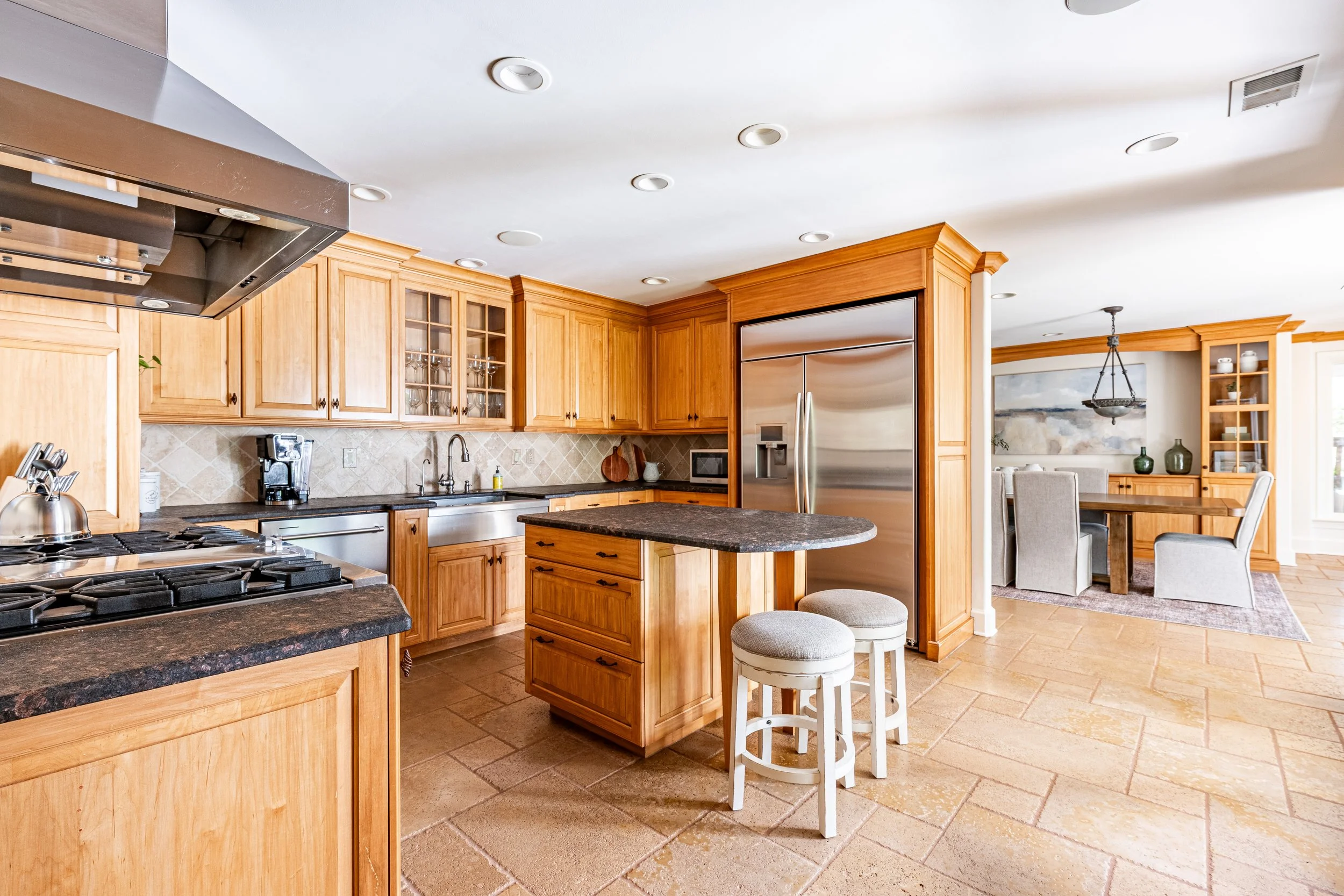 Kitchen with wooden cabinets, black countertops, stainless steel appliances, small island, and barstools