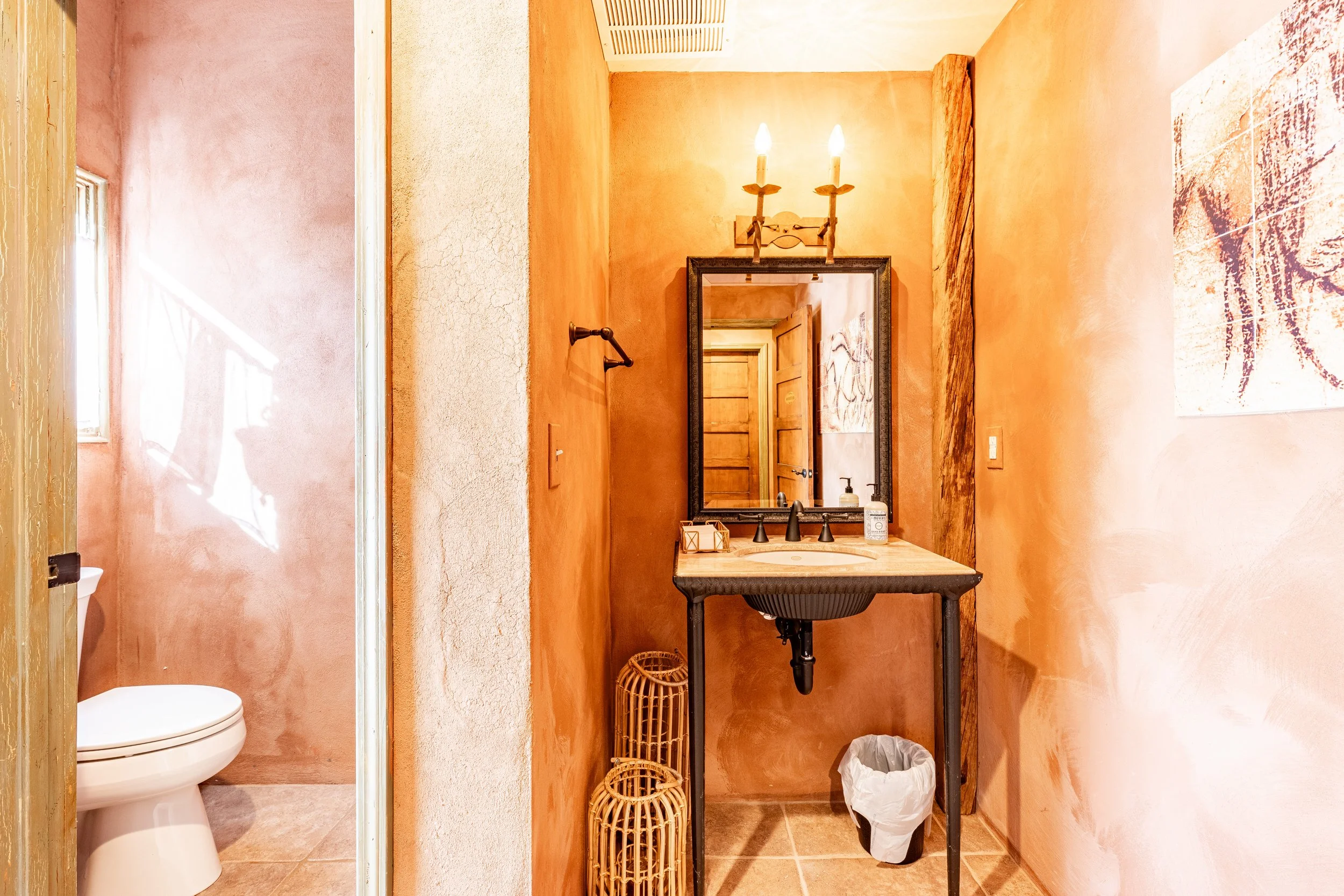 Bathroom with a small vanity, mirror, light fixture, and a separate toilet area visible through an open door.