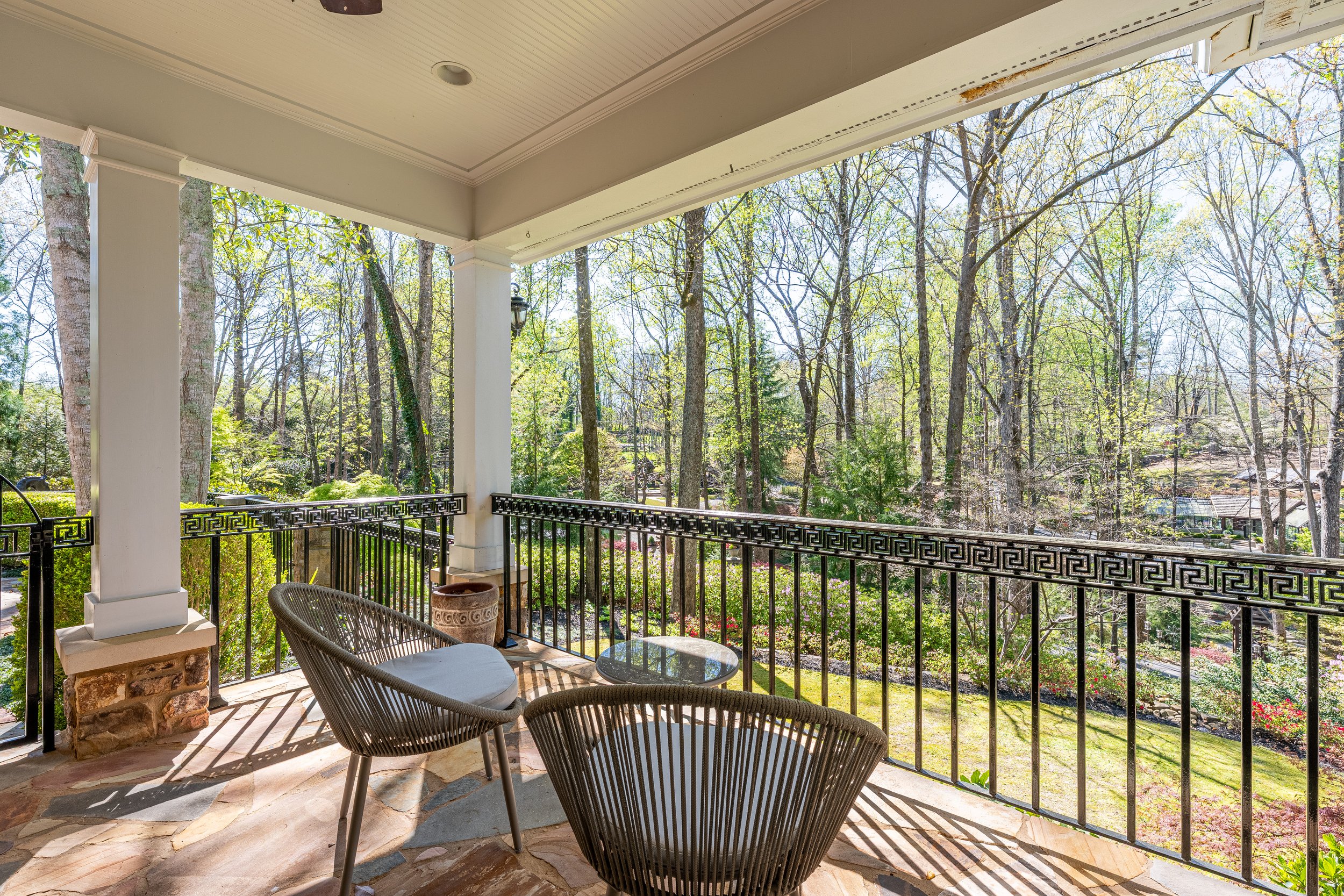 View from a porch with two woven chairs and a small round table, overlooking a lush forest with tall trees and spring foliage.