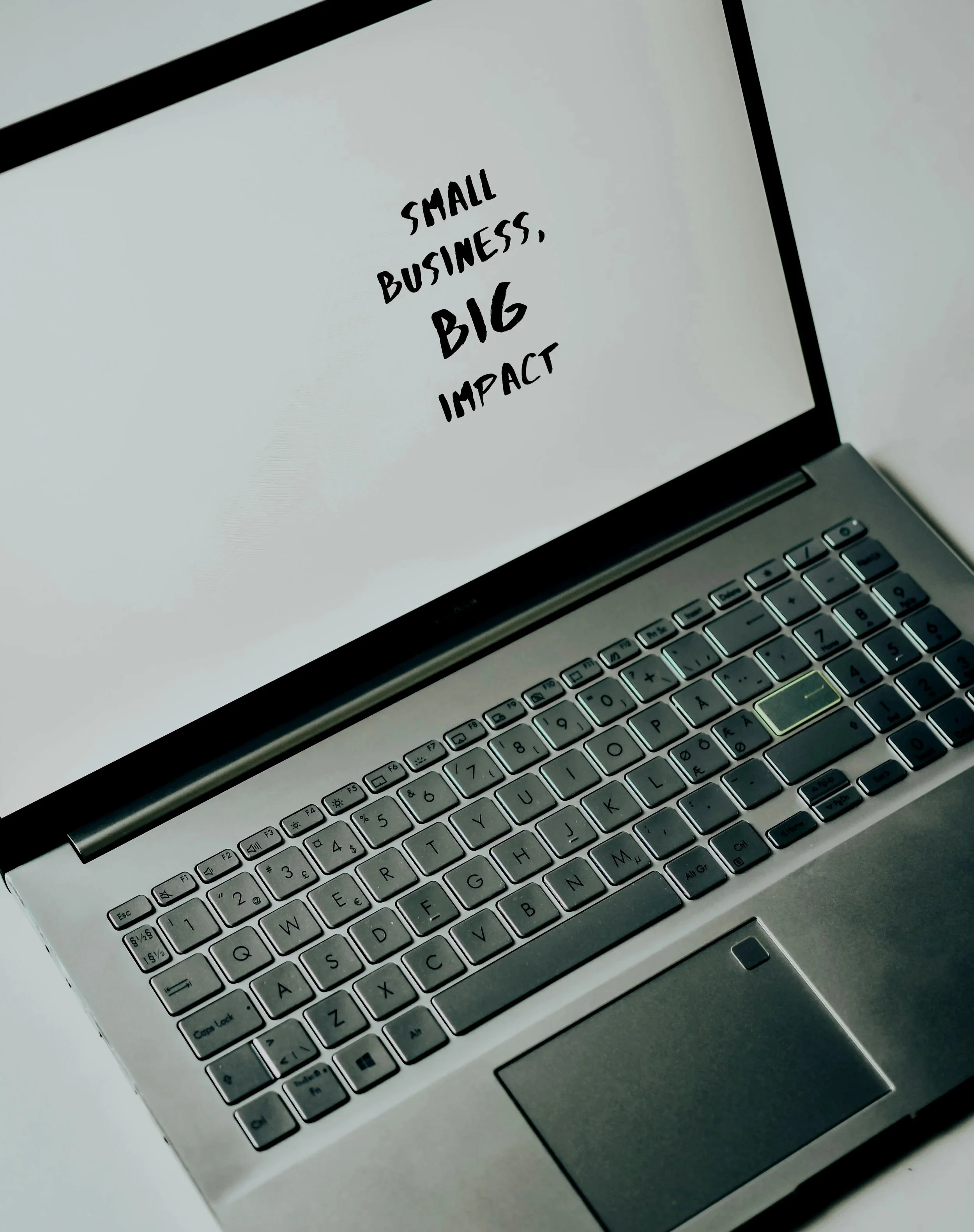 Laptop with the screen displaying the text 'Small Business, Big Impact' in black font.