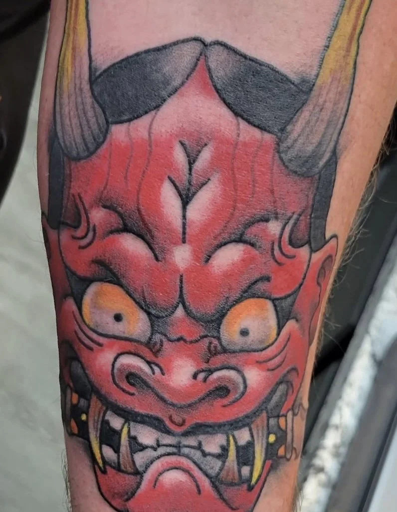 Tattoo of a traditional Japanese-style demon with red face, large teeth, pointy ears, and fierce expression.