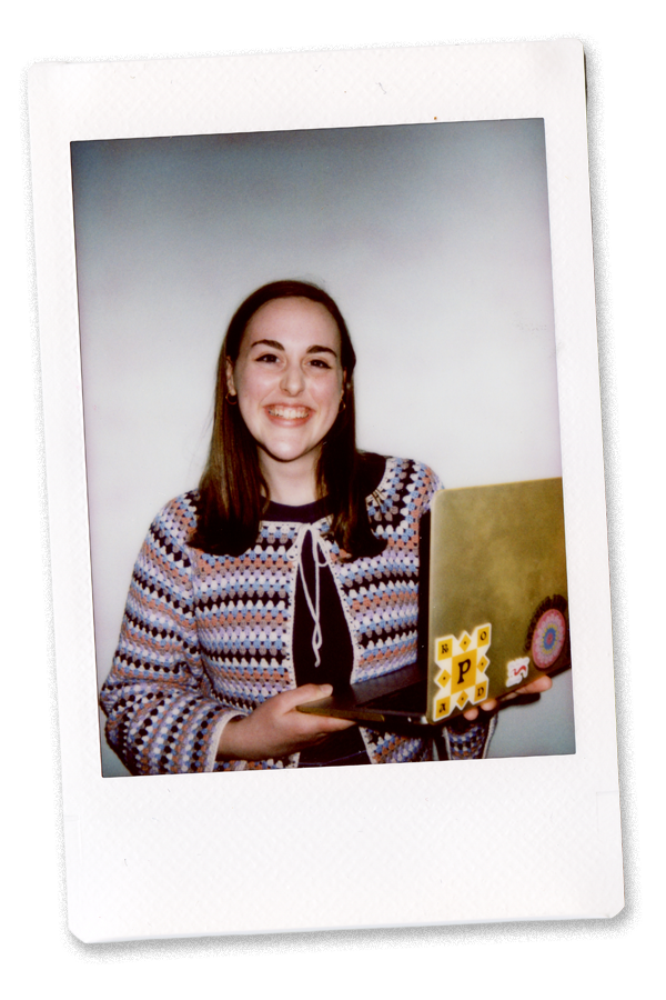 A young woman smiling, holding a laptop with decorative stickers, against a white background.