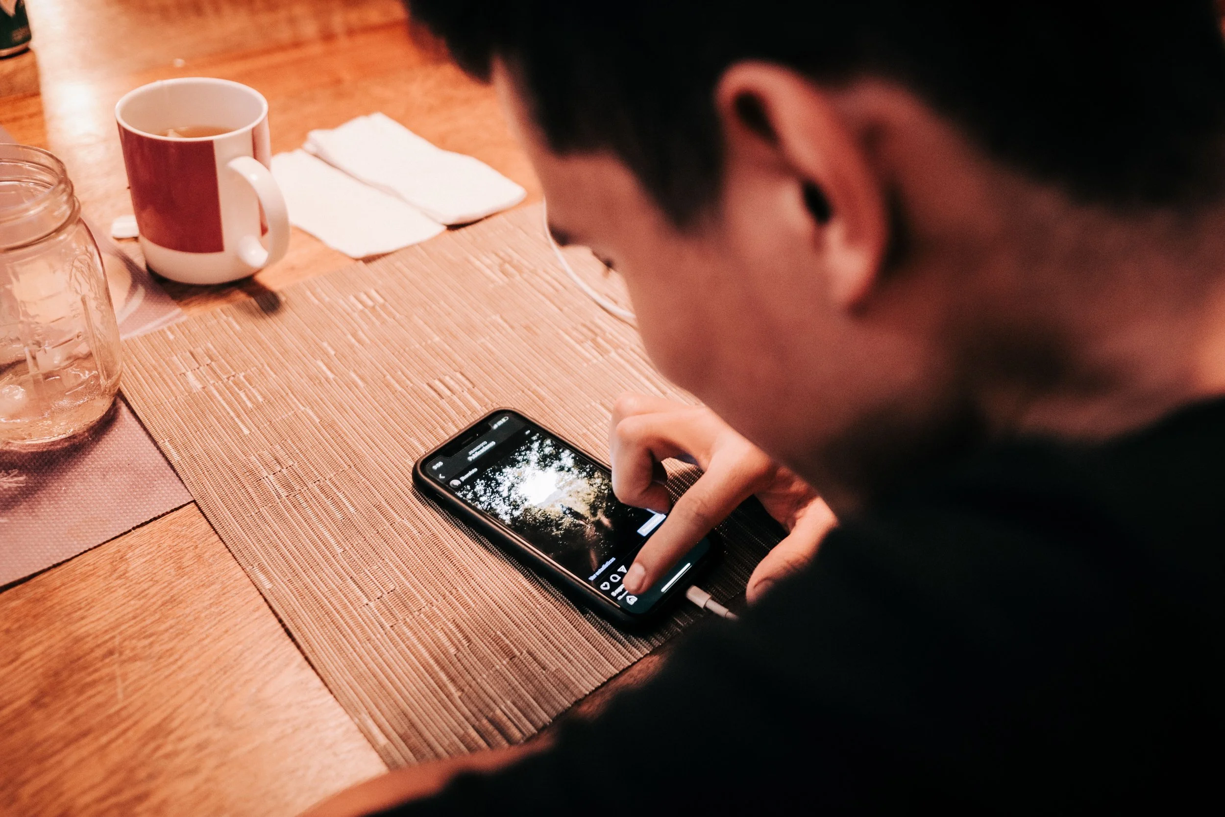 A man pauses with his hand beside a smartphone on a wooden table.