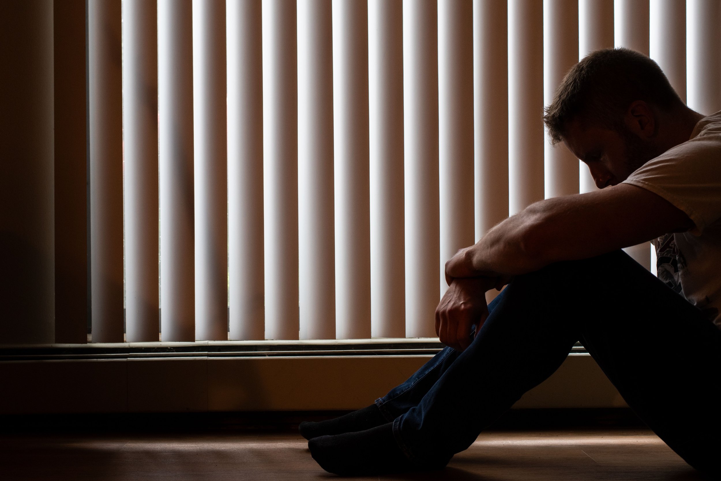 Silhouette of a man sitting quietly beside window blinds.