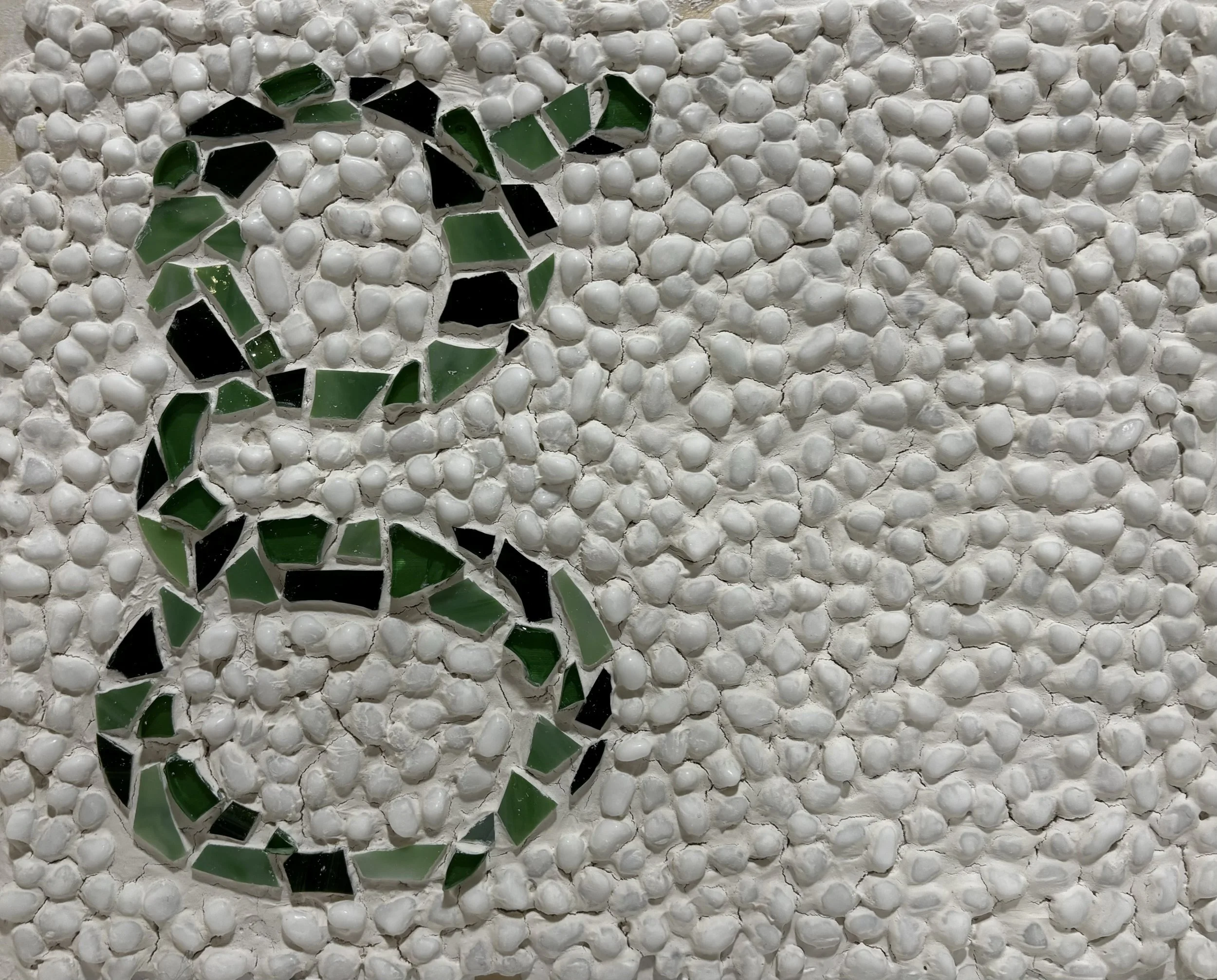 Mosaic pattern with a large letter 'S' made of green and black tiles on a white pebble background.