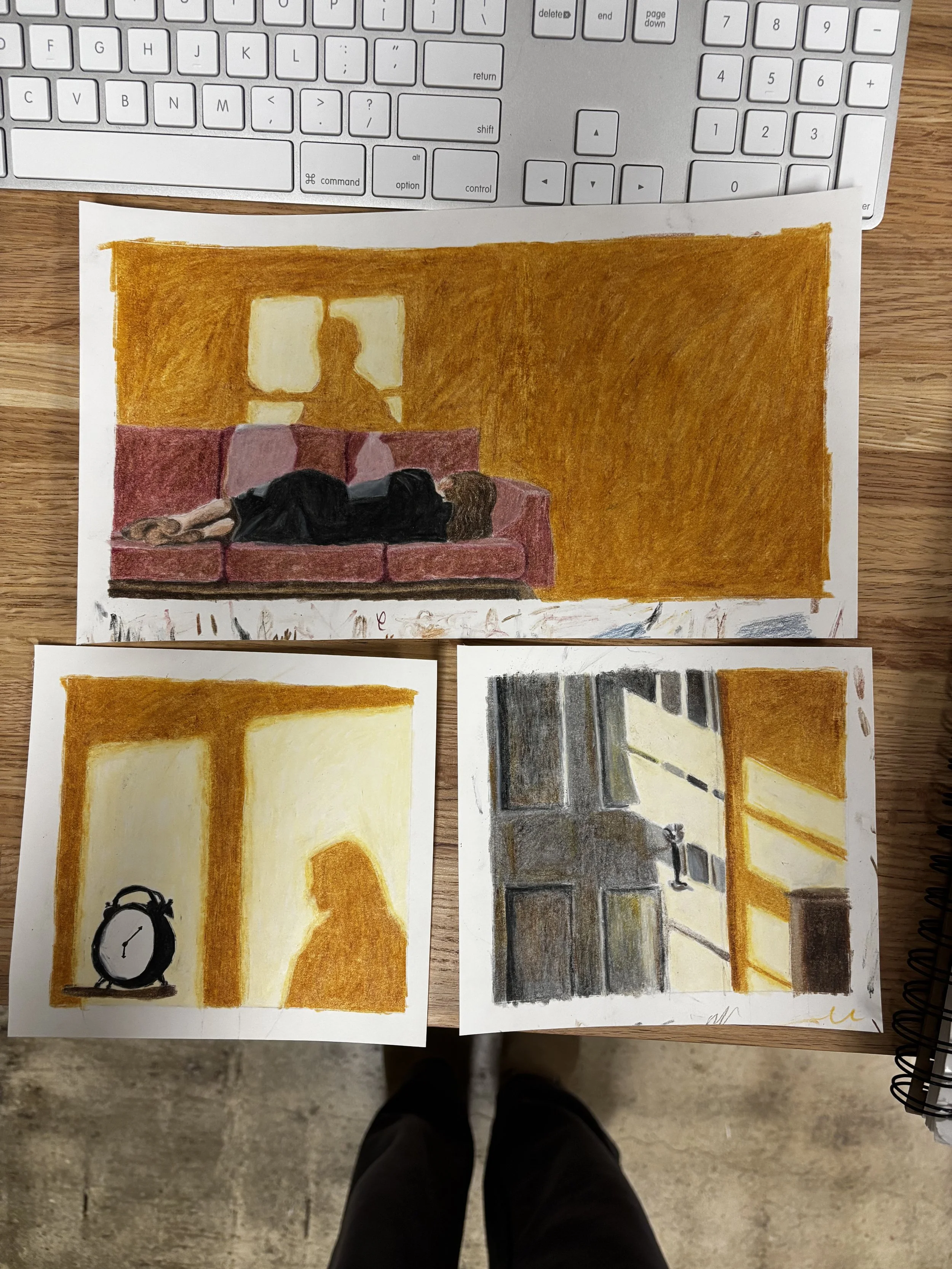 Three colored sketches of diffused indoor scenes are placed on a wooden table with a white keyboard at the top. The sketches depict a person lying on a couch with a yellow wall behind, a silhouette of a woman standing near a lamp with a clock on a table, and a view of a building with windows and shadows, illuminated by warm sunlight.