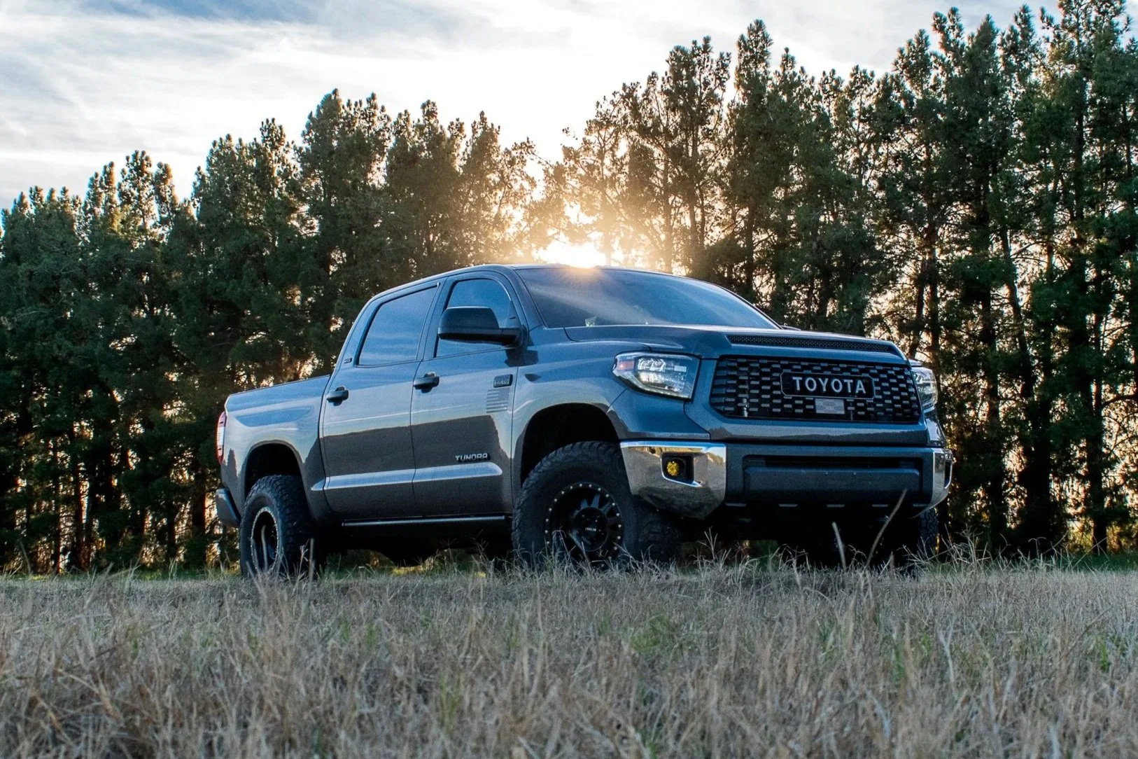 A dark blue Toyota Tundra pickup truck parked in a grassy field with trees in the background during sunset.